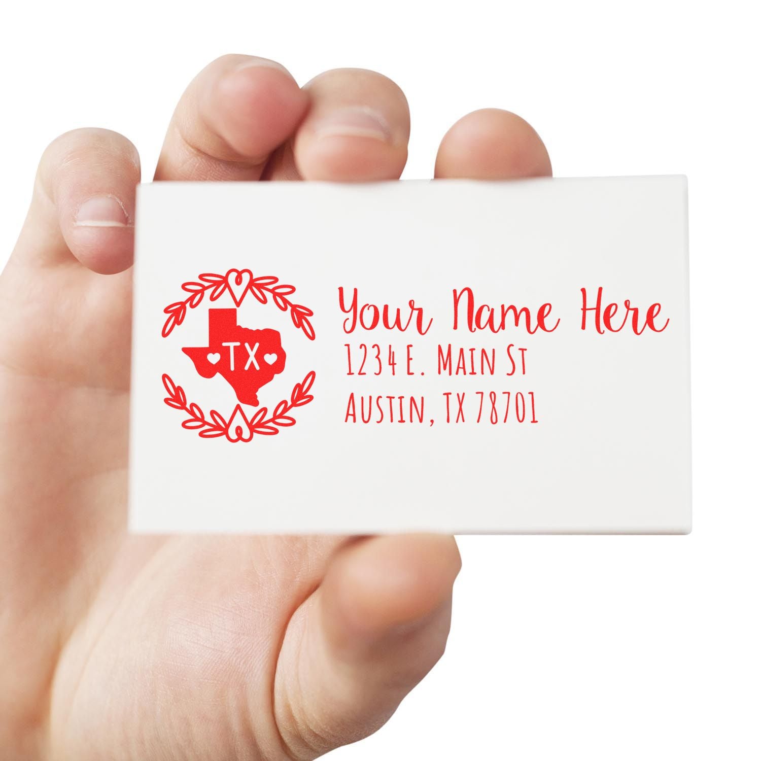 Hand holding a card stamped with the Self-Inking State Wreath of Texas Address Stamp, featuring a red Texas outline with hearts and address text in red.