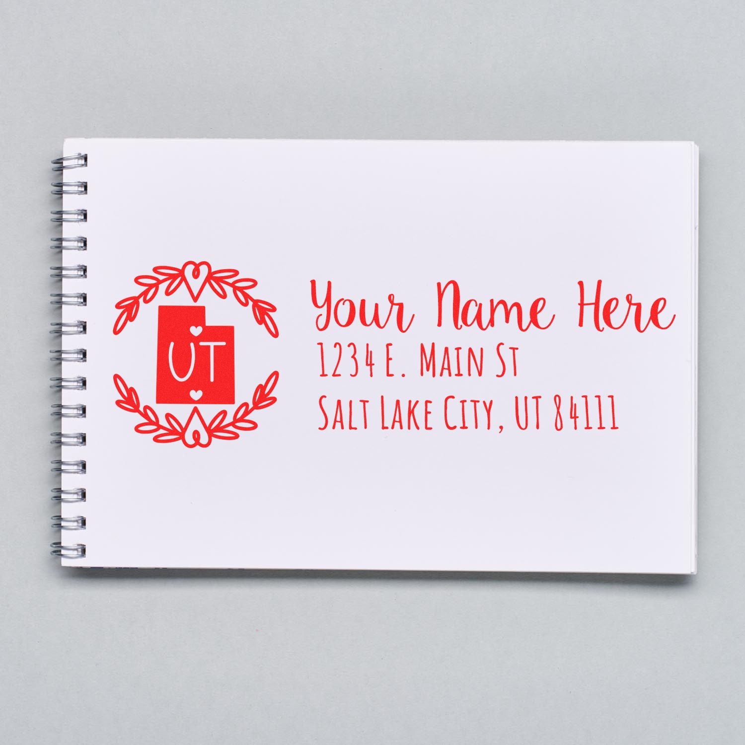 Utah State Custom Return Address Stamp on a white notebook, featuring a red design with UT and placeholder text for name and address in Salt Lake City, UT.