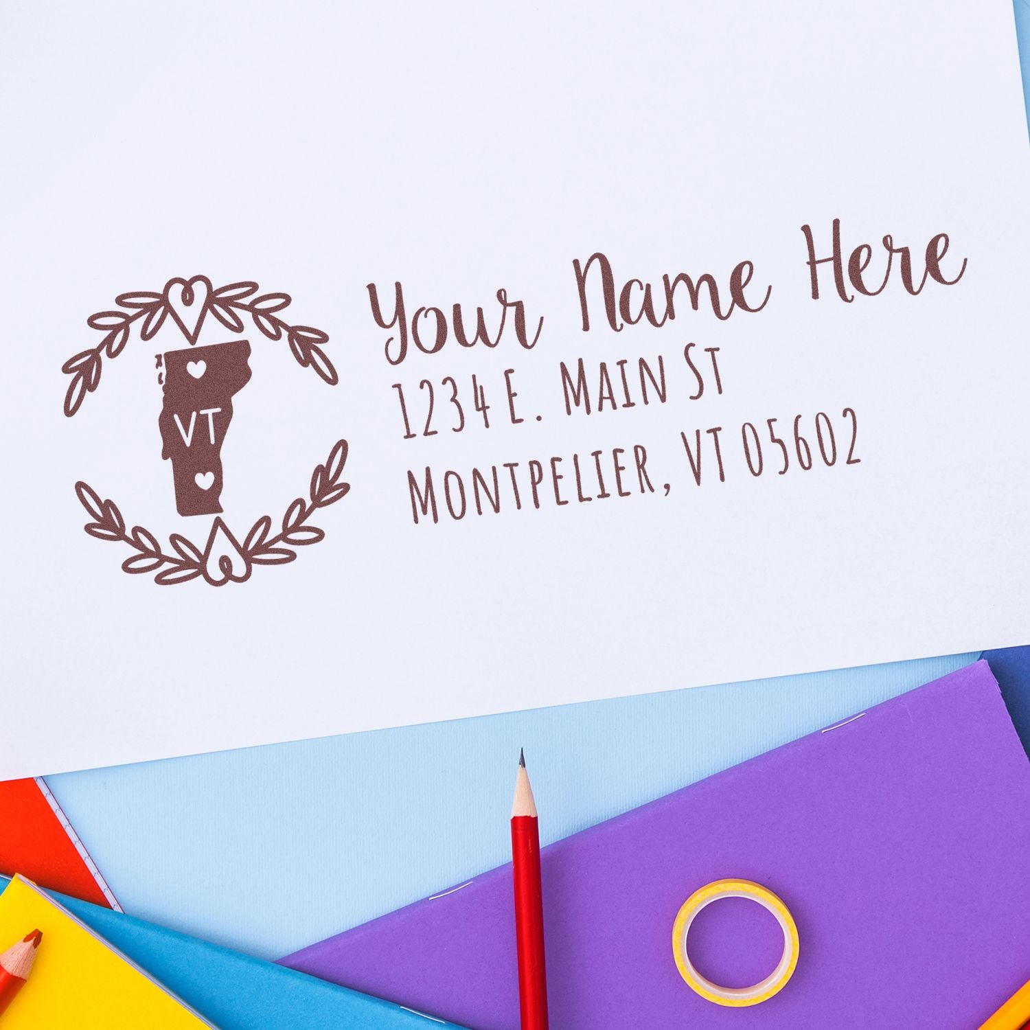 Vermont State Custom Return Address Stamp on white paper with a decorative border, featuring a Vermont map design. Surrounded by colorful stationery, including a red pencil and purple folders.