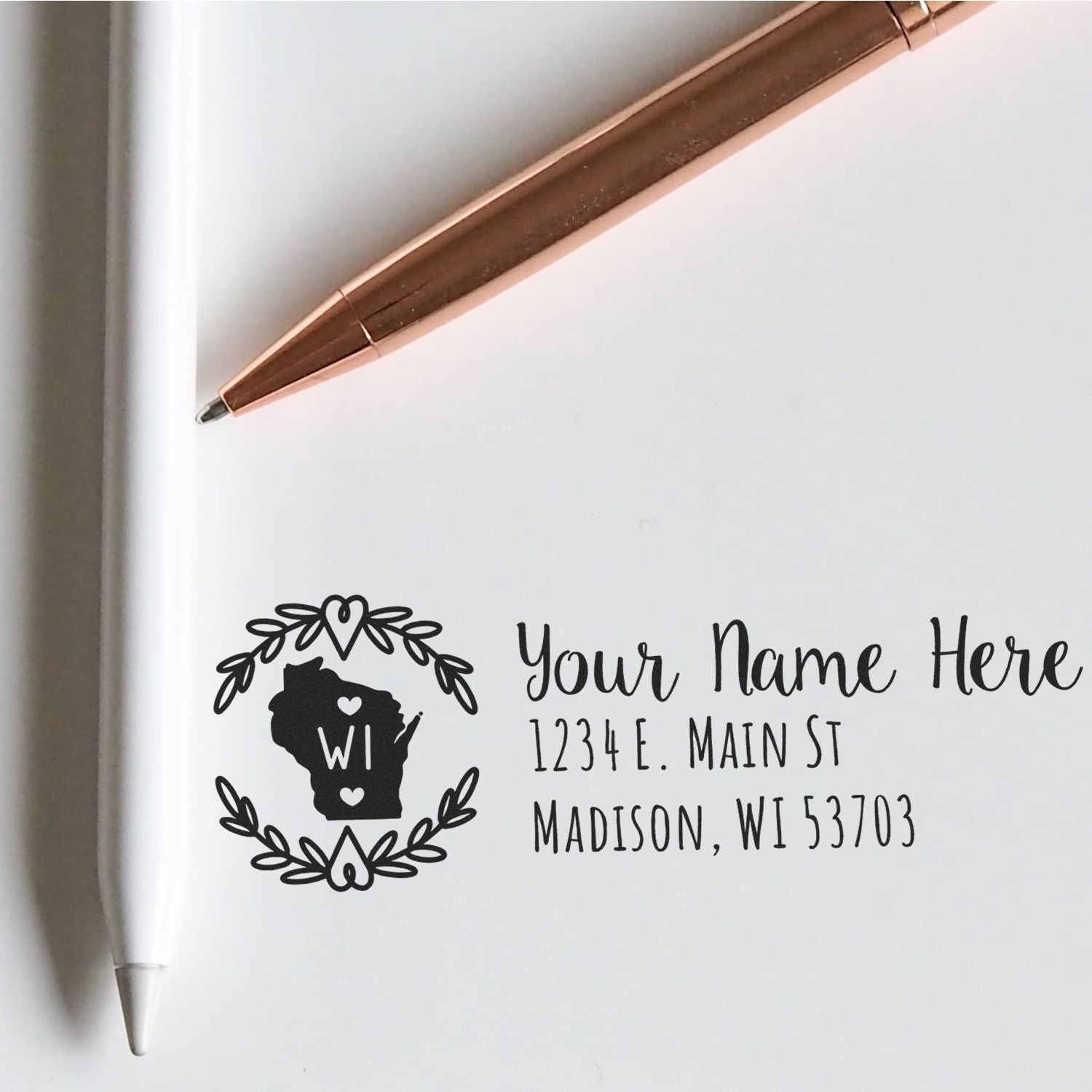 Wisconsin State Custom Return Address Stamp on white paper with a rose gold pen. Features a state outline with heart design and customizable address text. Ideal for personalizing mail.