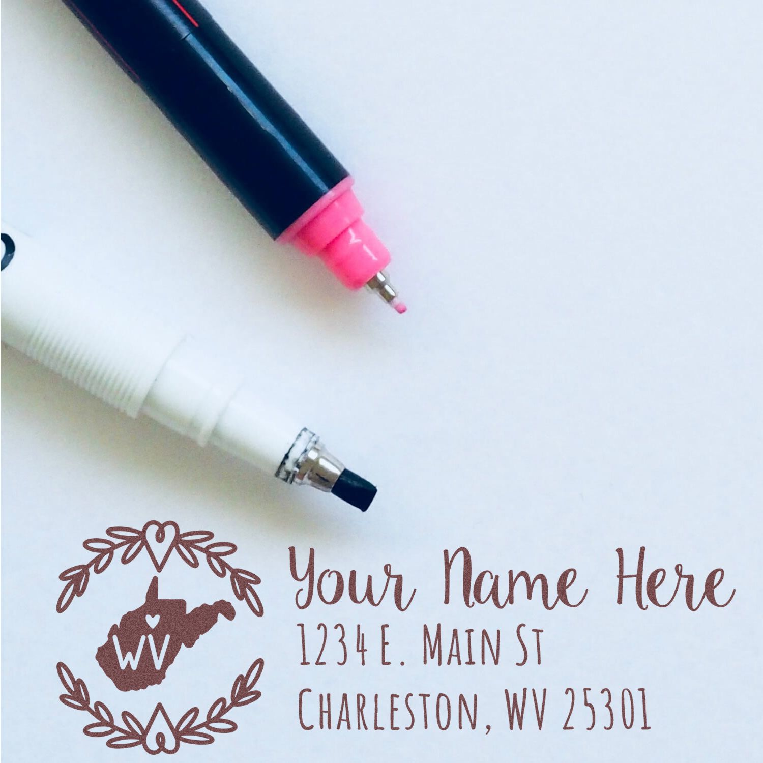 West Virginia State Custom Return Address Stamp displayed with two pens. The stamp features a decorative state outline and customizable address text, perfect for personalizing mail.