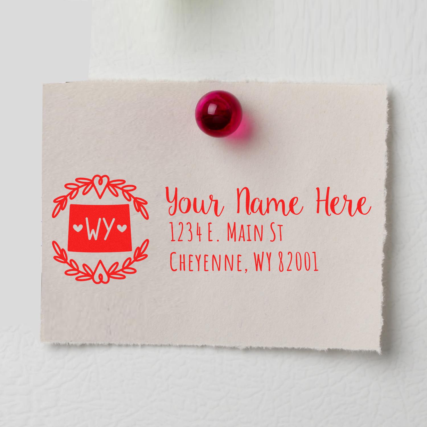 Self-Inking State Wreath of Wyoming Address Stamp on a note with a red pin, featuring a decorative wreath design and sample address text in red.