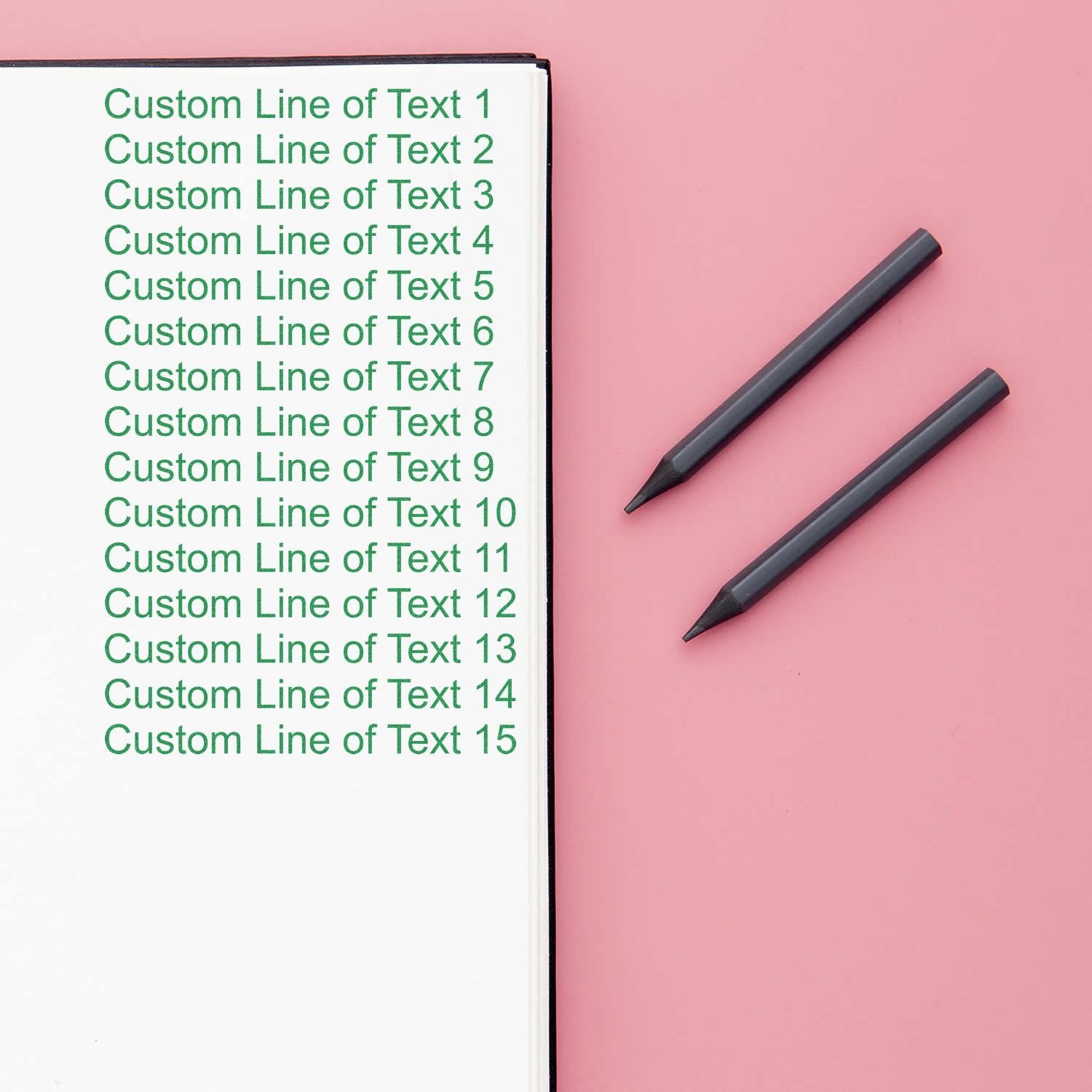 15-Line Custom Rubber Stamp with Wood Handle in use, stamping green text on white paper, with two black pens on a pink background.