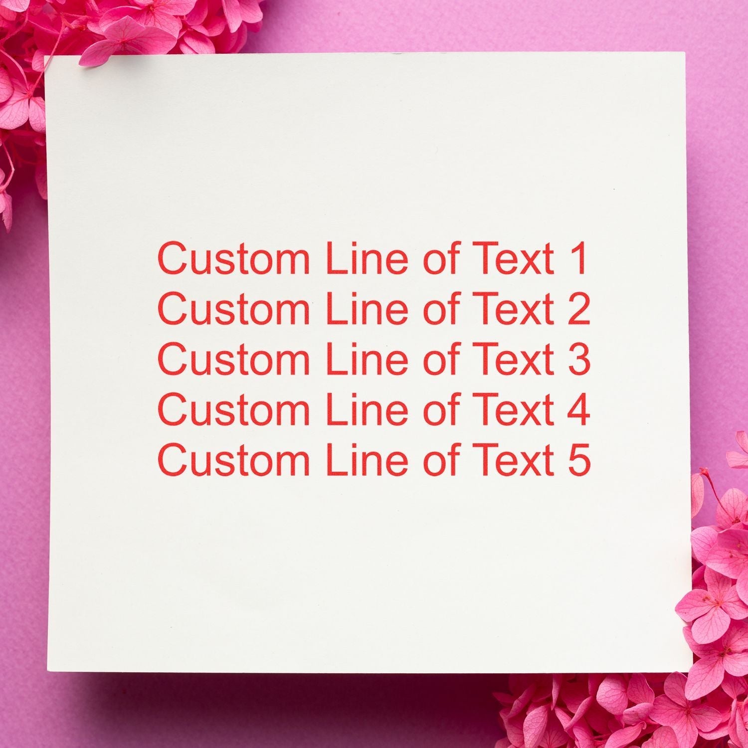 A 5 Line Custom Rubber Stamp with Wood Handle imprints red text on white paper, surrounded by pink flowers on a pink background.