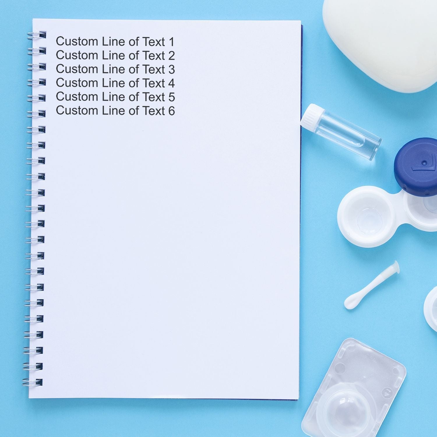 6 Line Custom Rubber Stamp with Wood Handle used on a spiral notebook, surrounded by contact lens accessories on a blue background.