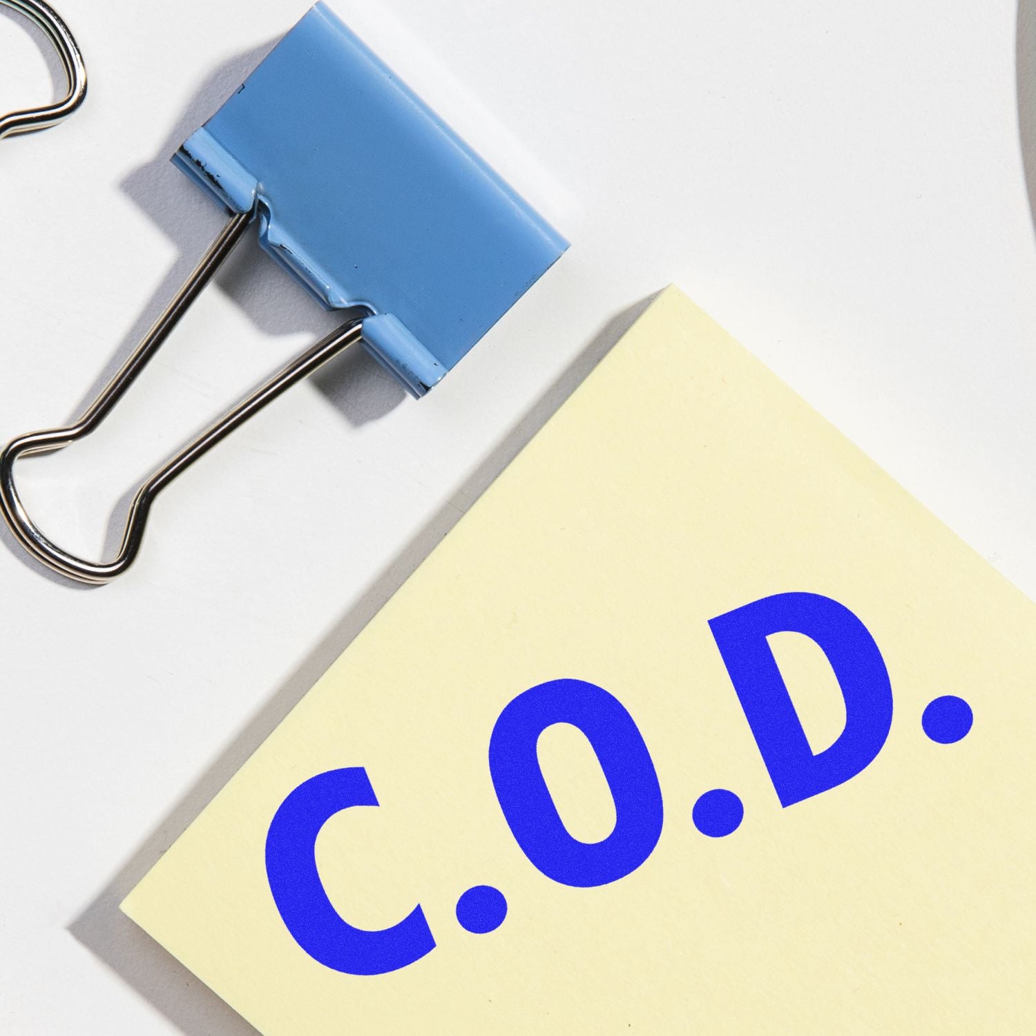 A blue Large Pre-Inked C.O.D. Stamp next to a blue binder clip and a yellow paper with C.O.D. printed in blue.