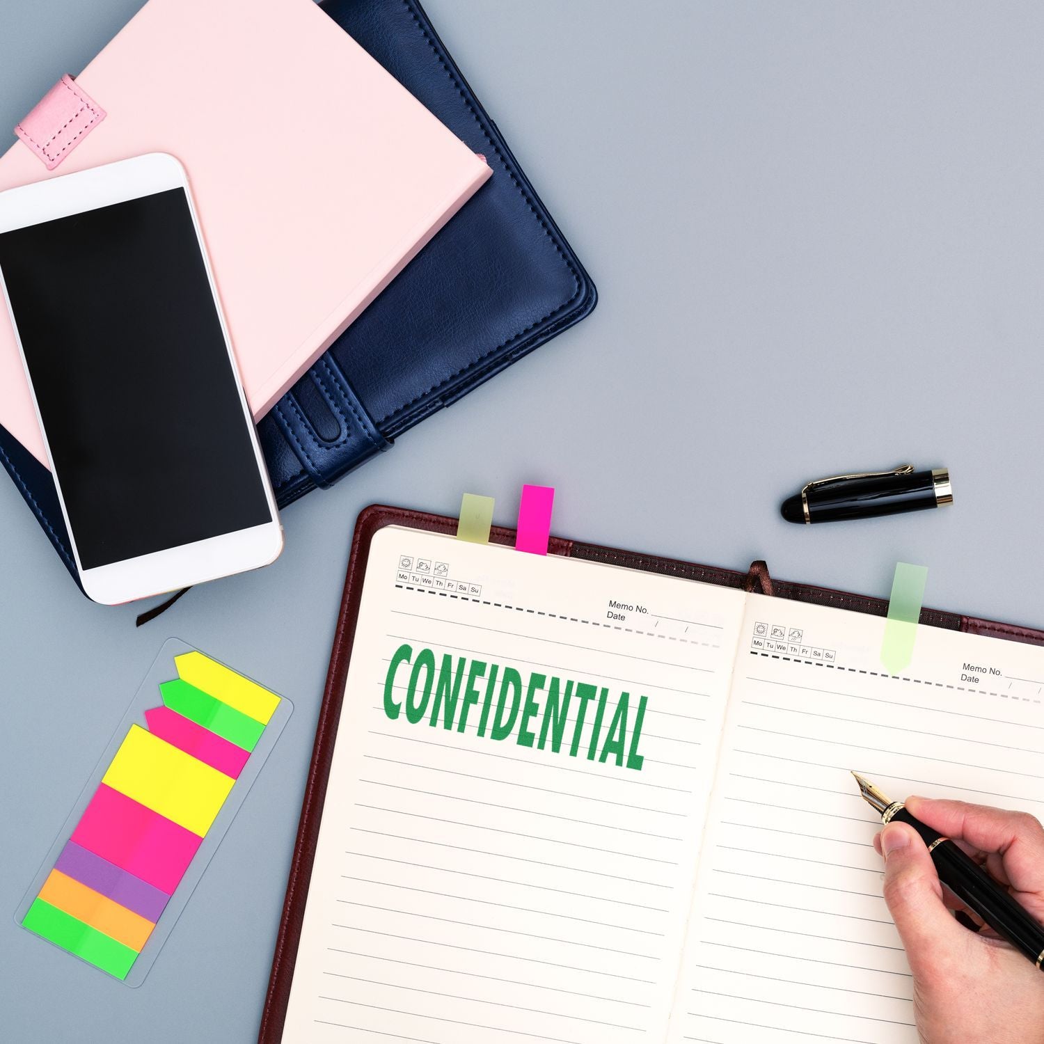 A desk with a Large Pre-Inked Confidential Stamp on a notebook, colorful sticky notes, a smartphone, and a pen.