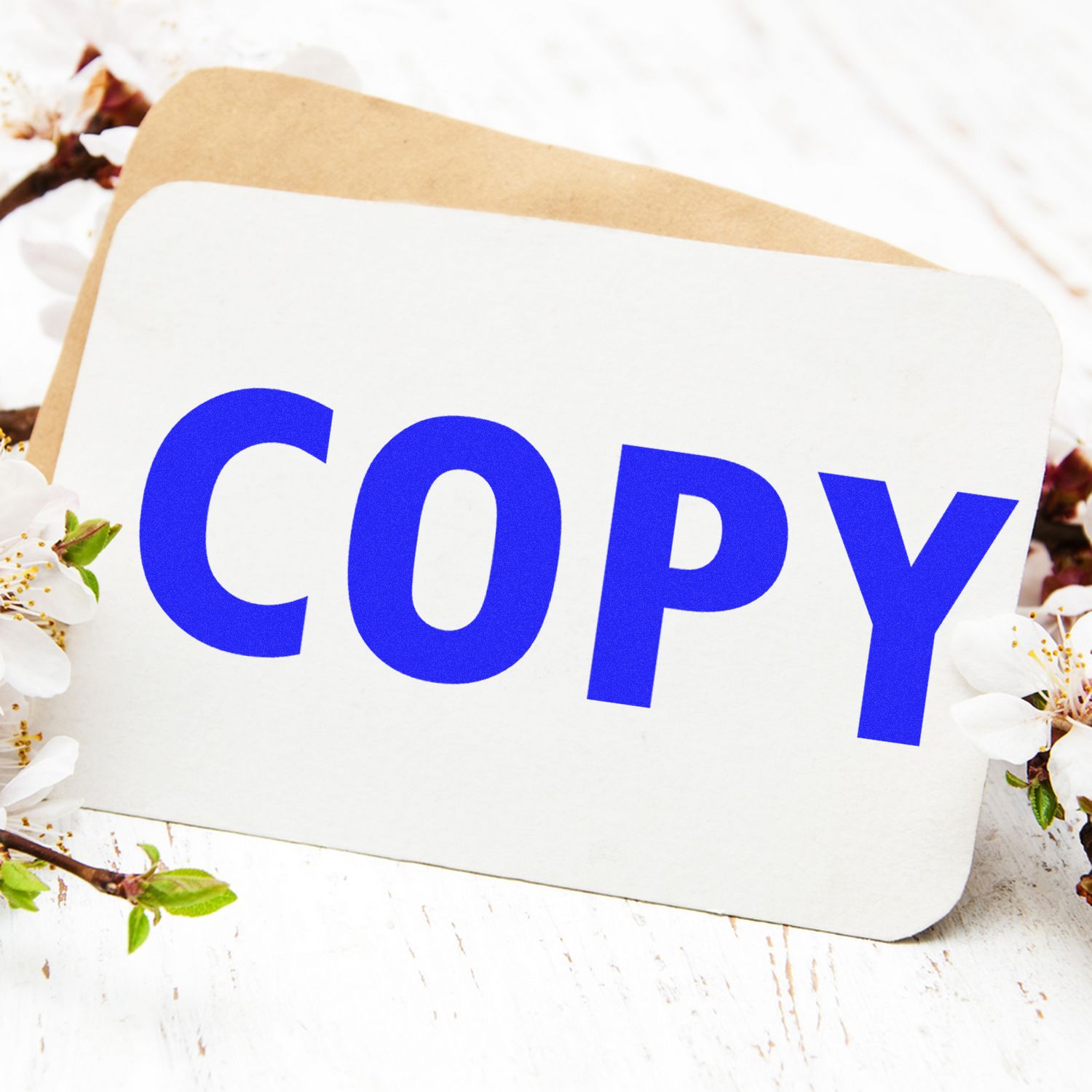 Large Pre-Inked Copy Stamp with bold blue COPY text on a white card, placed on a wooden surface with flowers in the background.