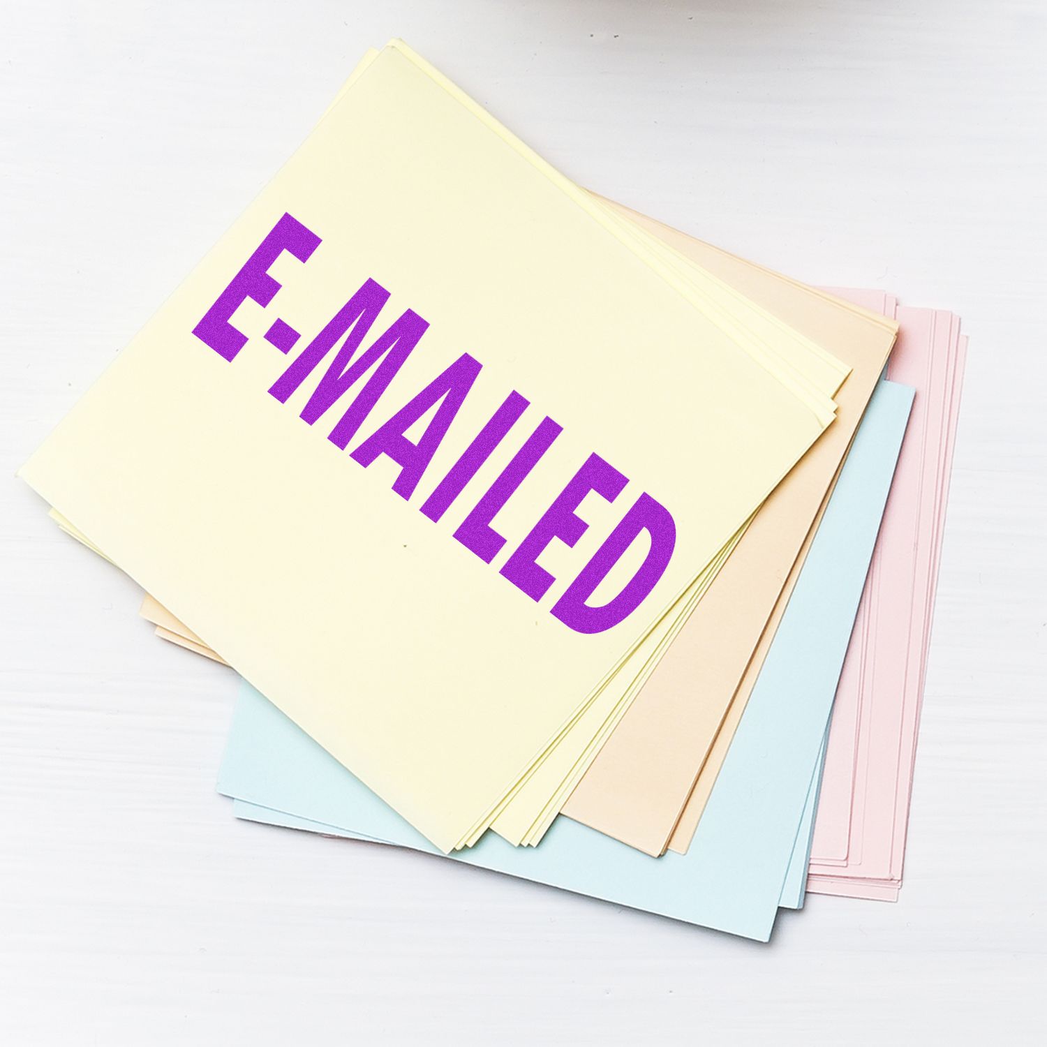 Stack of papers stamped with E-MAILED using the Large Pre-Inked E-Mailed Stamp, featuring bold purple text on pastel-colored sheets.