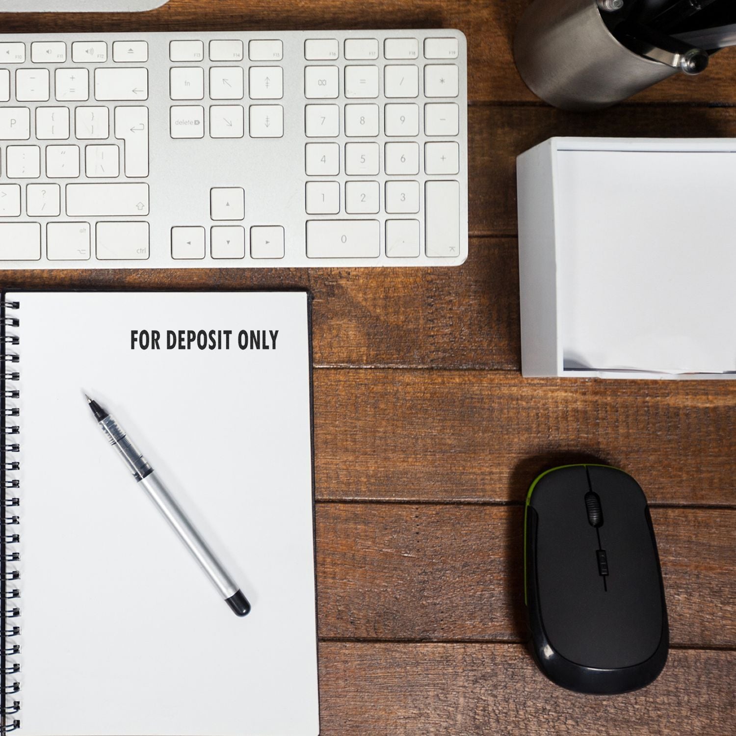 Large Pre-Inked For Deposit Only Stamp on a notebook, with a pen, keyboard, mouse, and office supplies on a wooden desk.