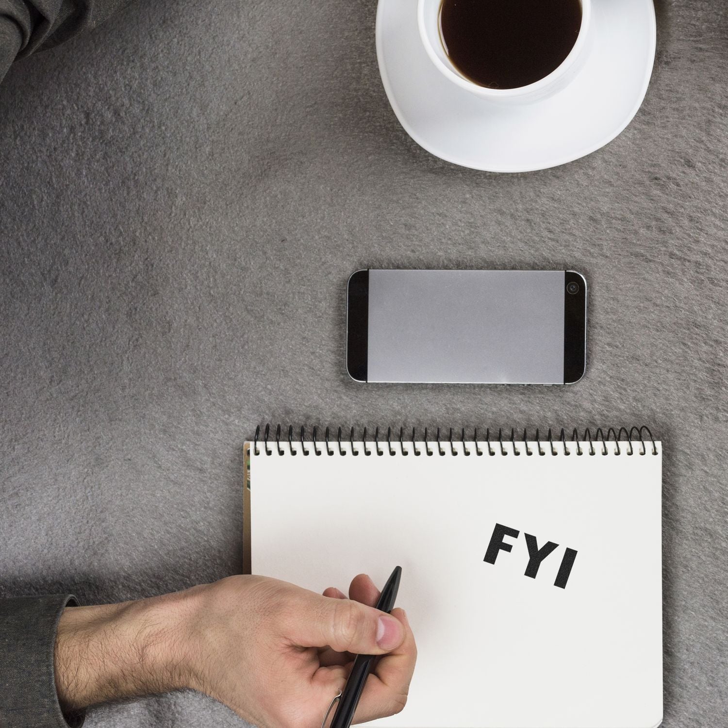 A hand holding a pen next to a notebook with FYI stamped on it using the Large Pre-Inked FYI Stamp, with a smartphone and coffee cup nearby.