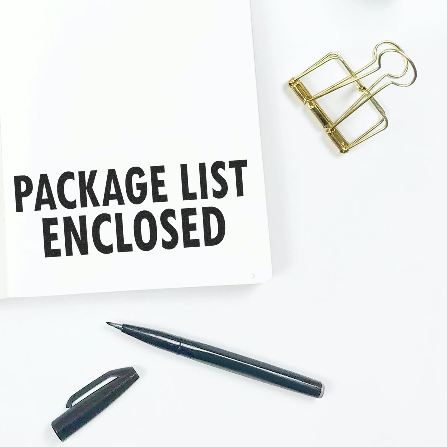 Large Pre-Inked Package List Enclosed Stamp on white paper, with a black pen, pen cap, and gold binder clip nearby on a white surface.