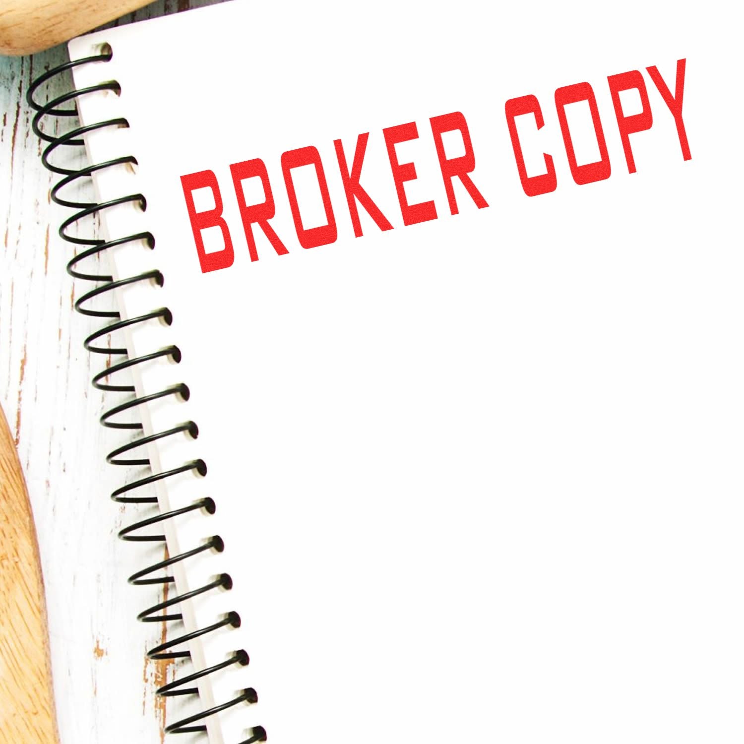 Large Pre-Inked Broker Copy Stamp in red ink on a white spiral notebook, placed on a wooden surface.