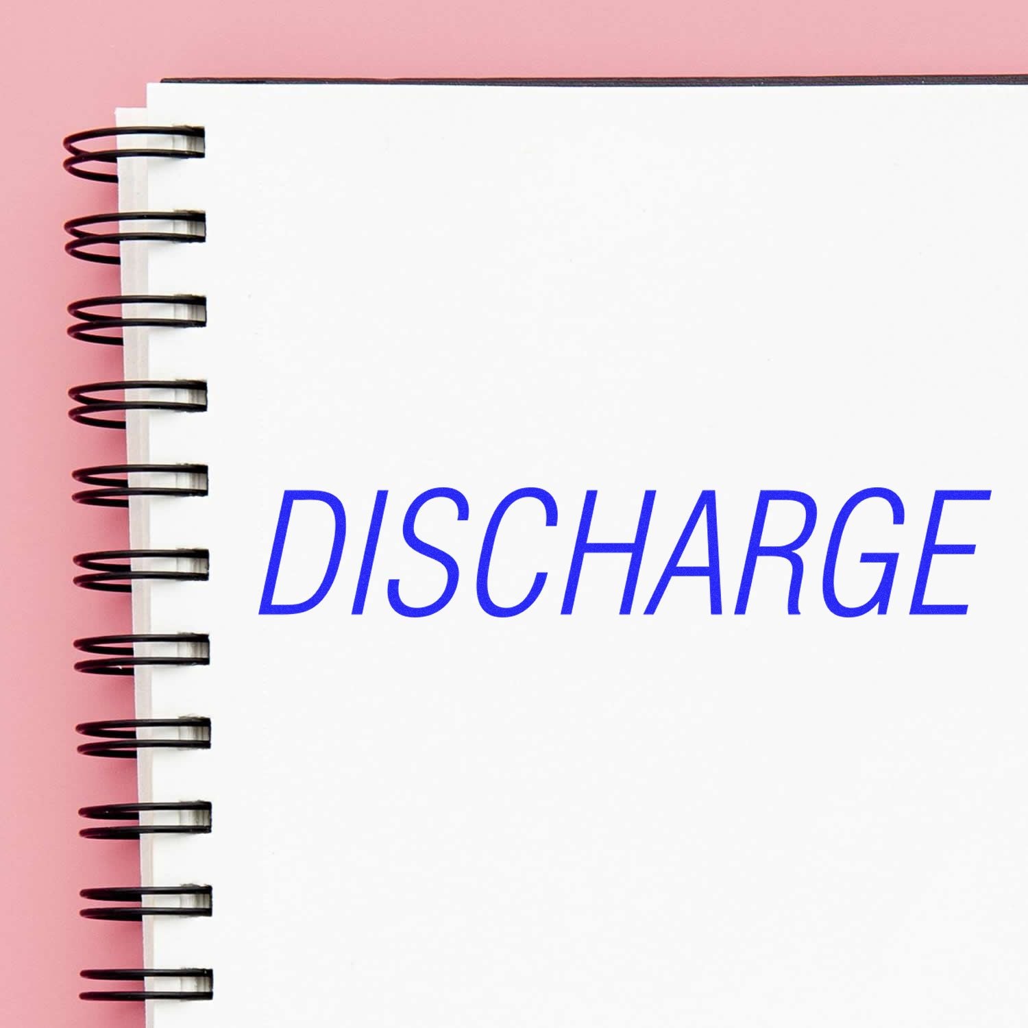 Large Pre-Inked Discharge Stamp imprinting the word DISCHARGE in blue ink on a white spiral-bound notebook with a pink background.