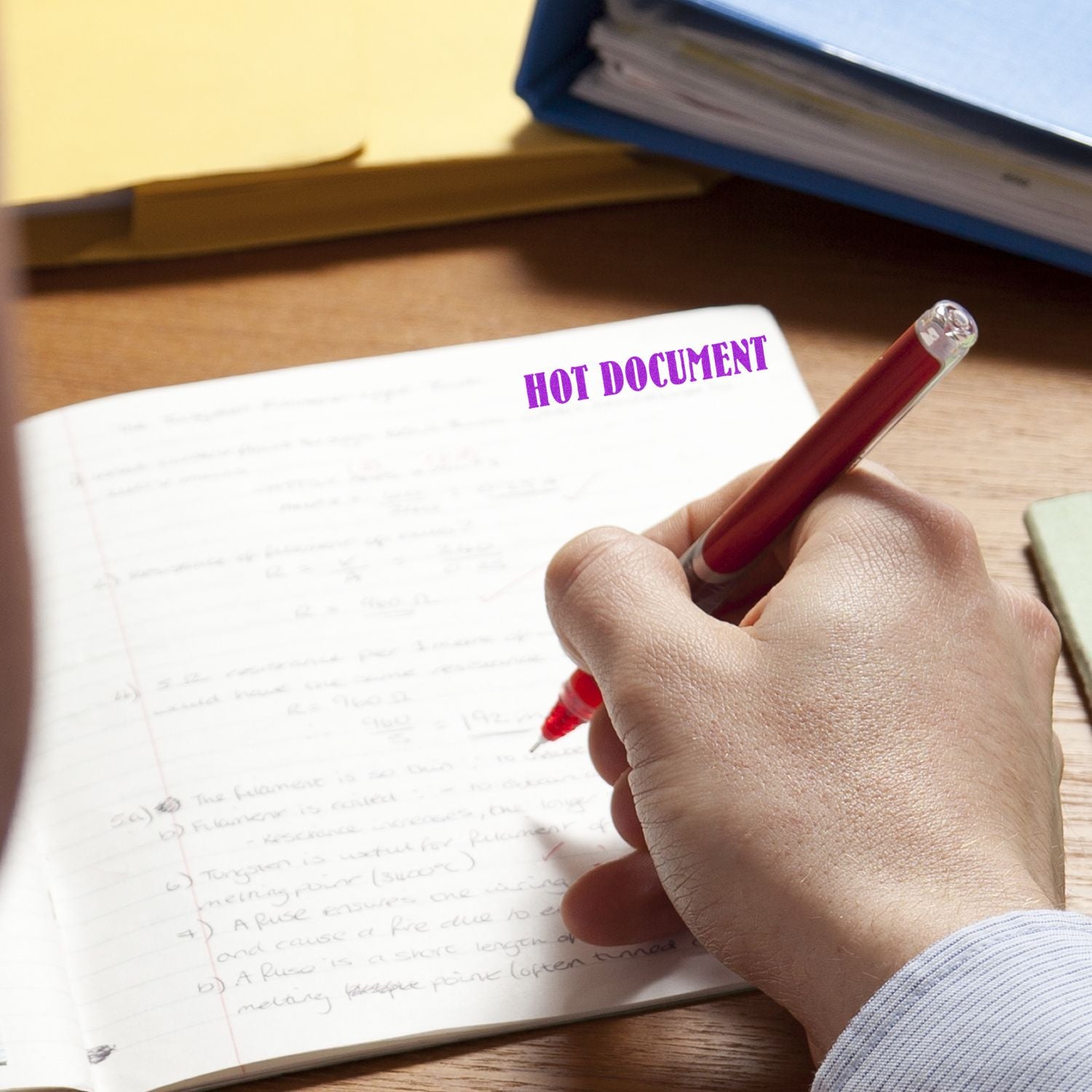 A hand using the Large Pre-Inked Hot Document Stamp on a notebook, with the text HOT DOCUMENT clearly visible in purple ink.