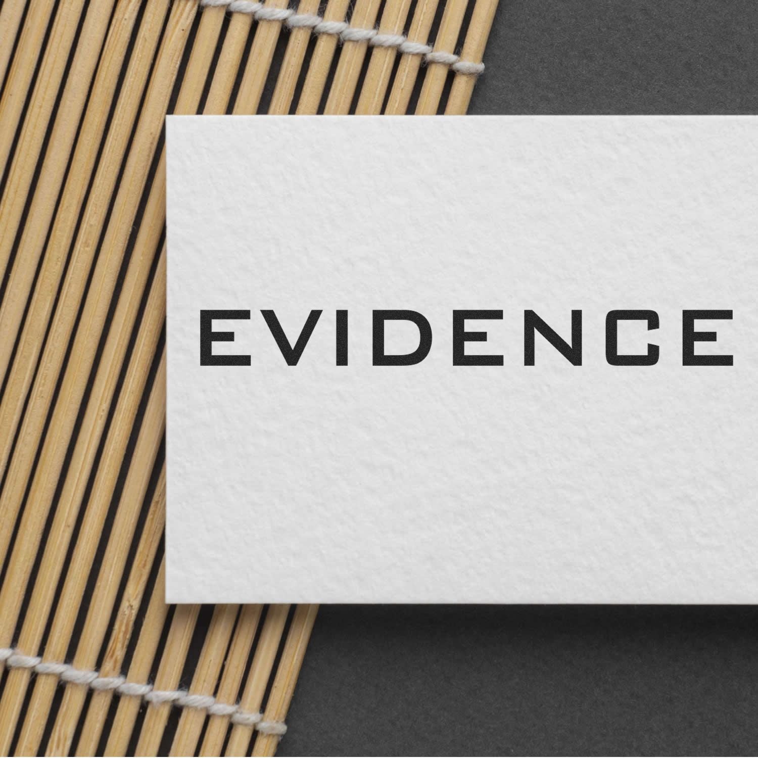 Large Pre-Inked Evidence Stamp imprint on white card, placed on a bamboo mat and dark background.