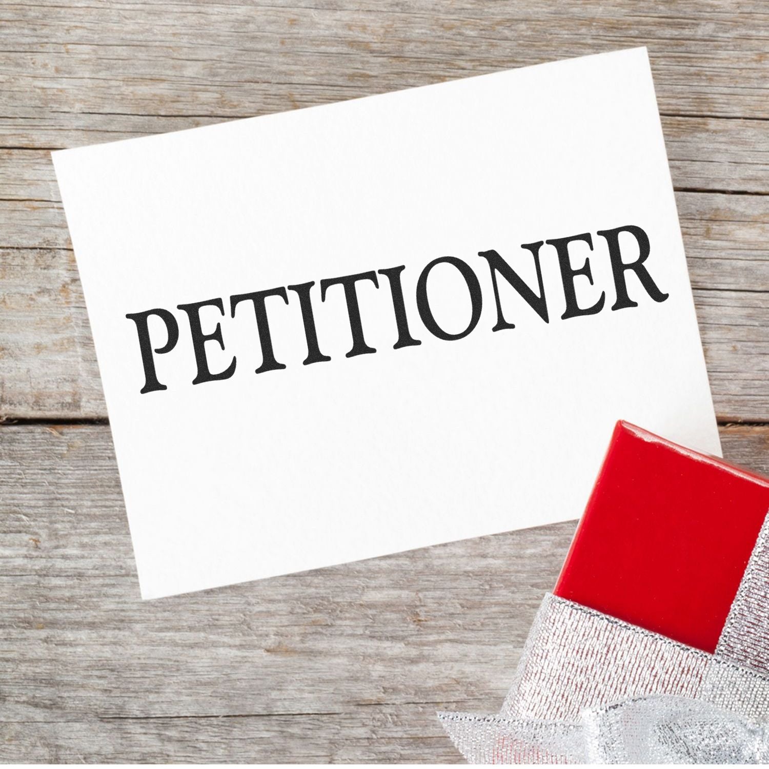 Large Pre-Inked Petitioner Stamp on white paper with PETITIONER text, placed on a wooden surface next to a red and silver gift box.