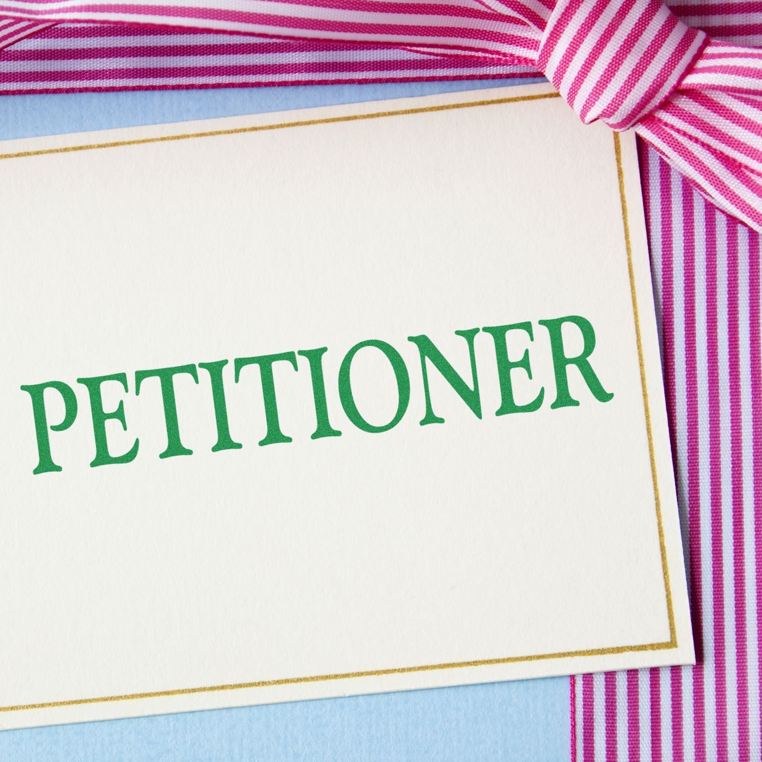 A card stamped with PETITIONER in green ink using the Large Pre-Inked Petitioner Stamp, placed on a pink and white striped ribbon background.