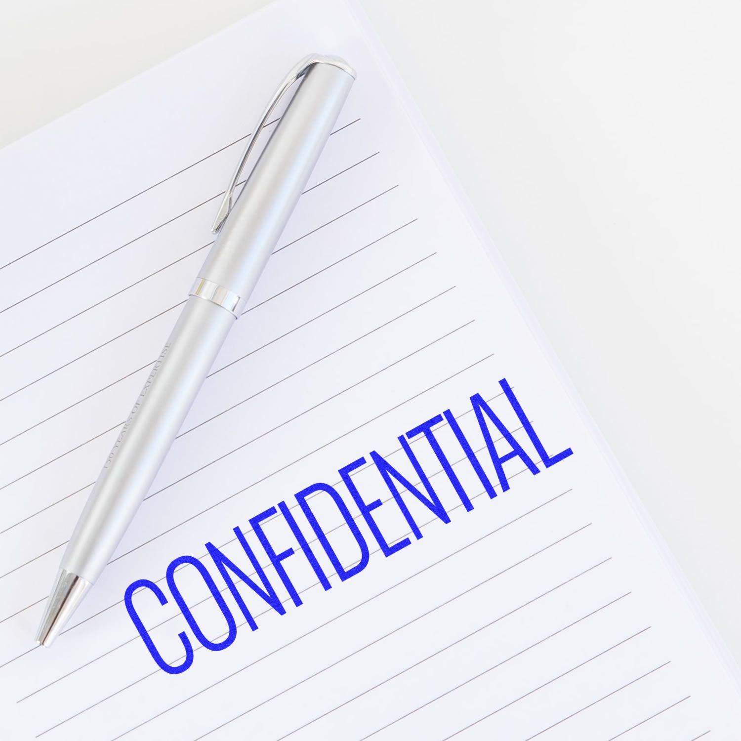 A notebook with CONFIDENTIAL stamped in blue ink using the Large Pre-Inked Narrow Font Confidential Stamp, next to a silver pen.