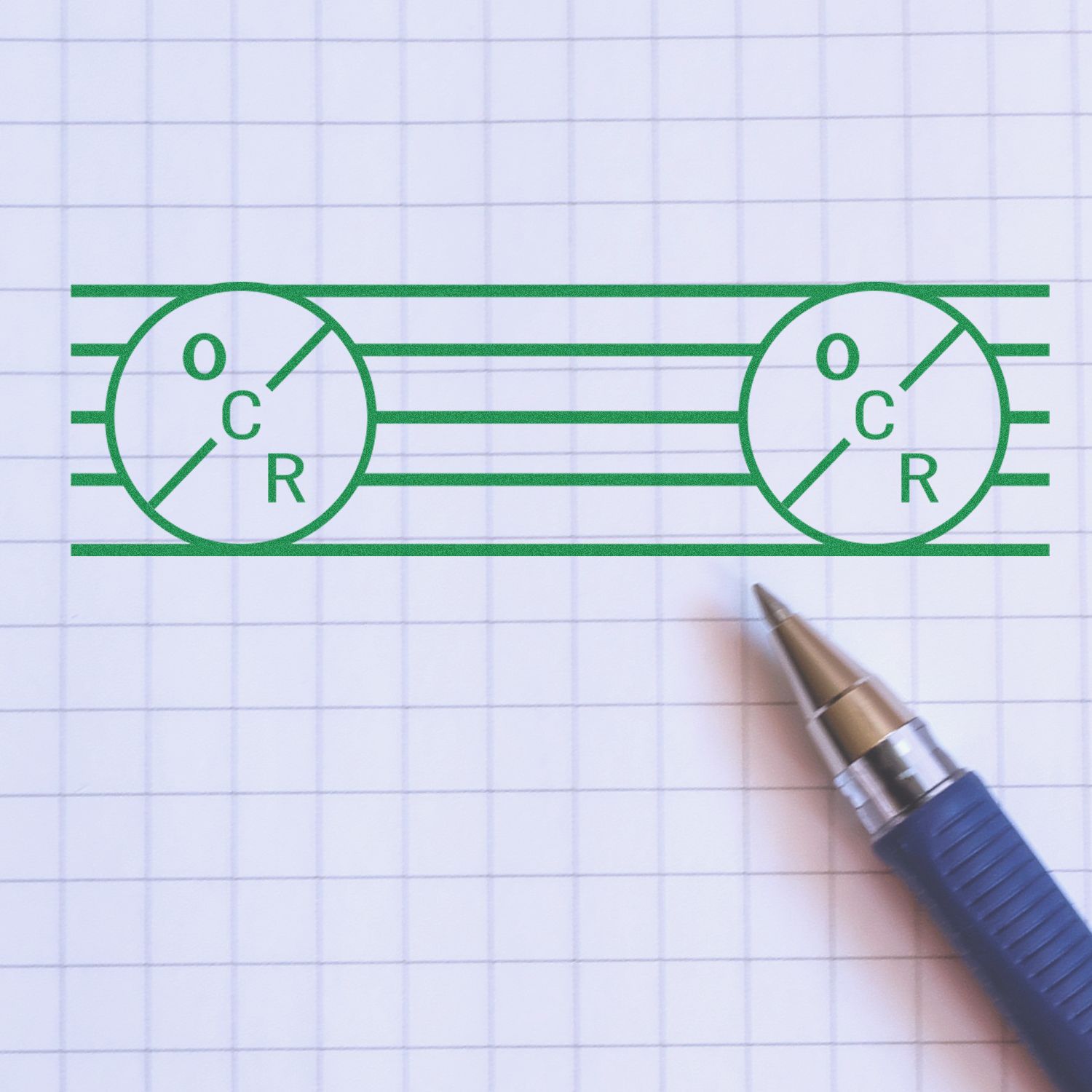 Large Pre-Inked OCR Stamp imprint in green ink on graph paper, with a blue pen placed at the bottom right corner.