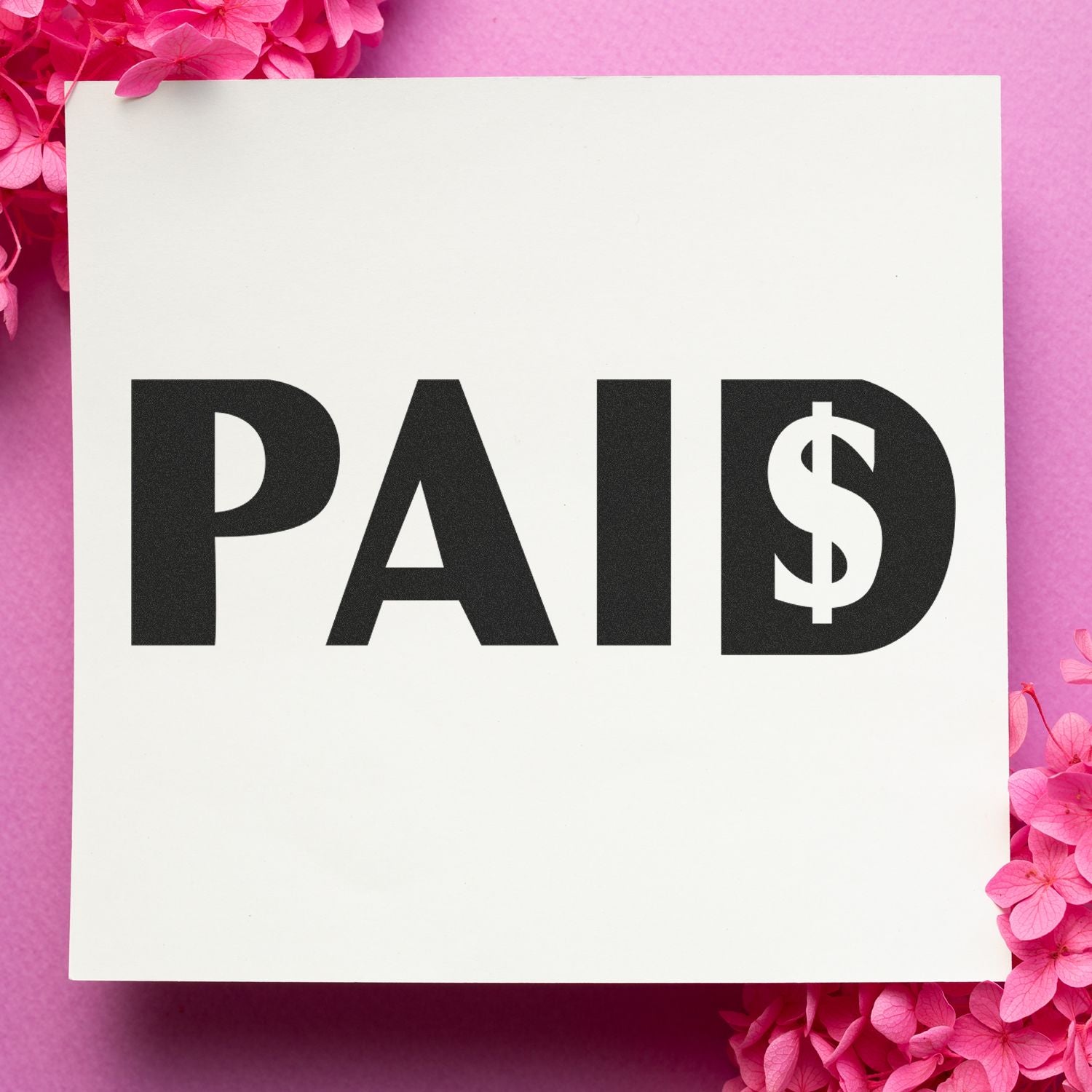 Large Pre-Inked Paid with Dollar Sign Stamp on white paper, surrounded by pink flowers, against a pink background.