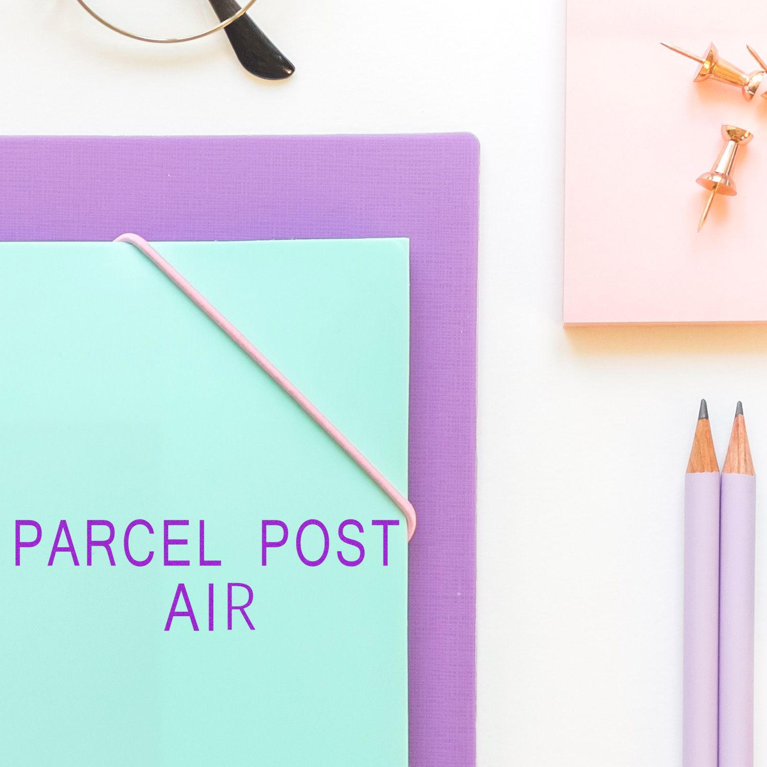 Large Pre-Inked Parcel Post Air Stamp on a mint green envelope with purple text, surrounded by office supplies on a white background.