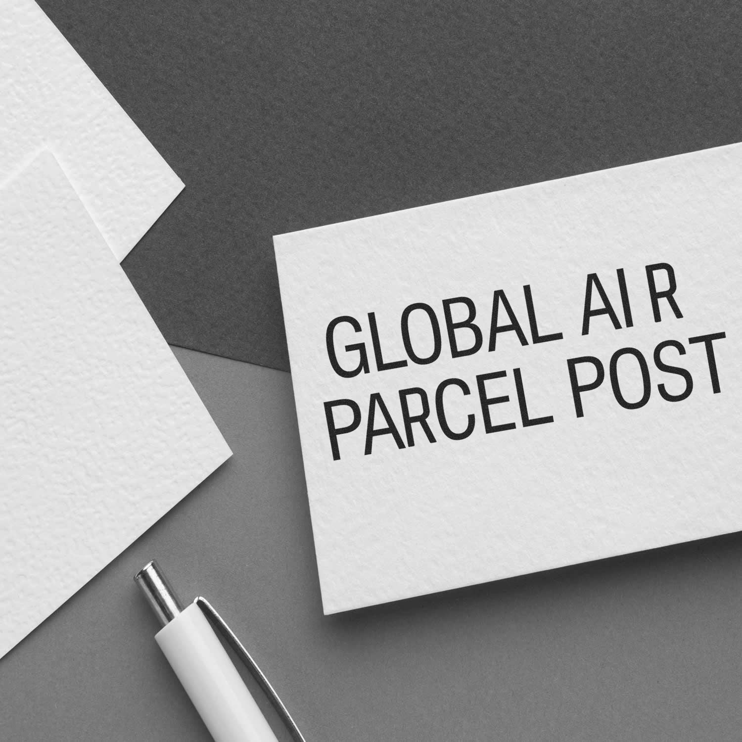 Large Pre-Inked Global Air Parcel Post Stamp on a white card with a pen and two blank cards on a gray background.