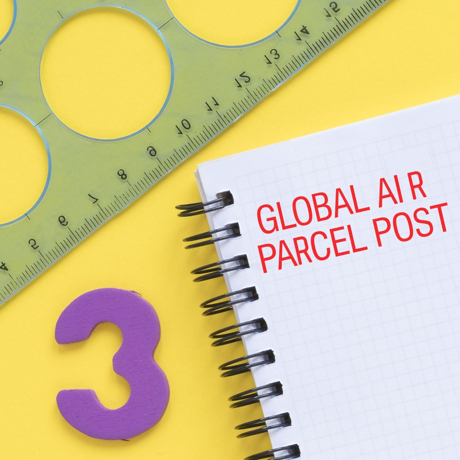 A Large Pre-Inked Global Air Parcel Post Stamp on a spiral notebook with a green ruler and a purple number 3 on a yellow background.