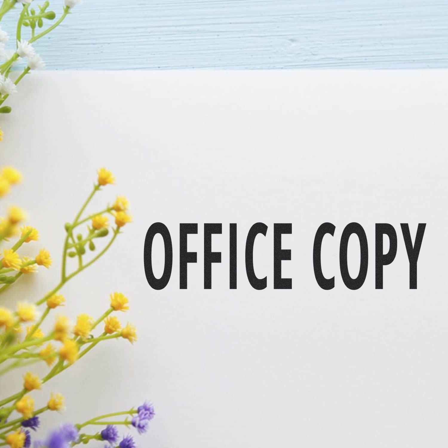 Large Pre-Inked Office Copy Stamp imprint on white paper with yellow and purple flowers on the side, against a light blue background.