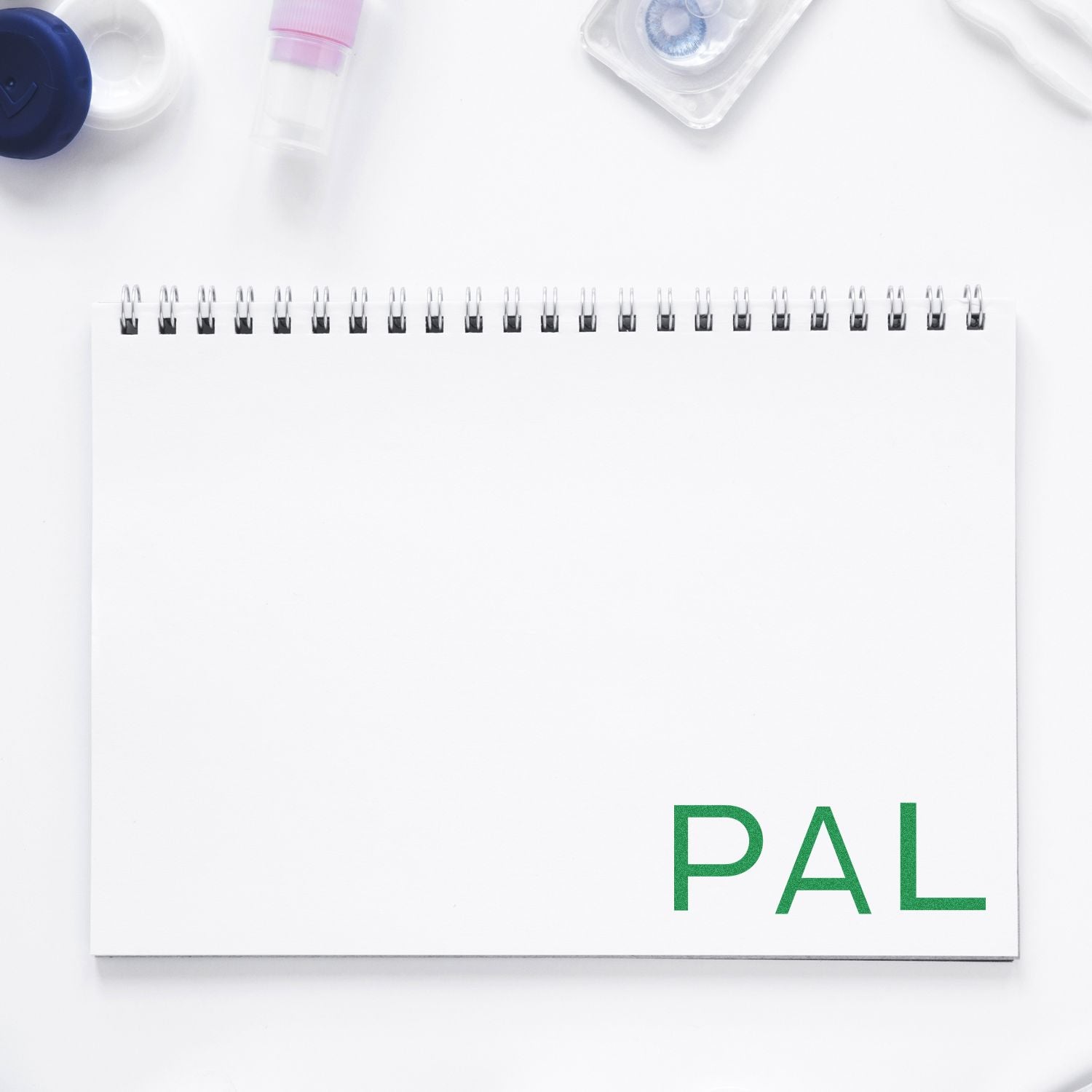 Large Pre-Inked PAL Stamp imprinting PAL in green on a white spiral notebook, surrounded by various office supplies.