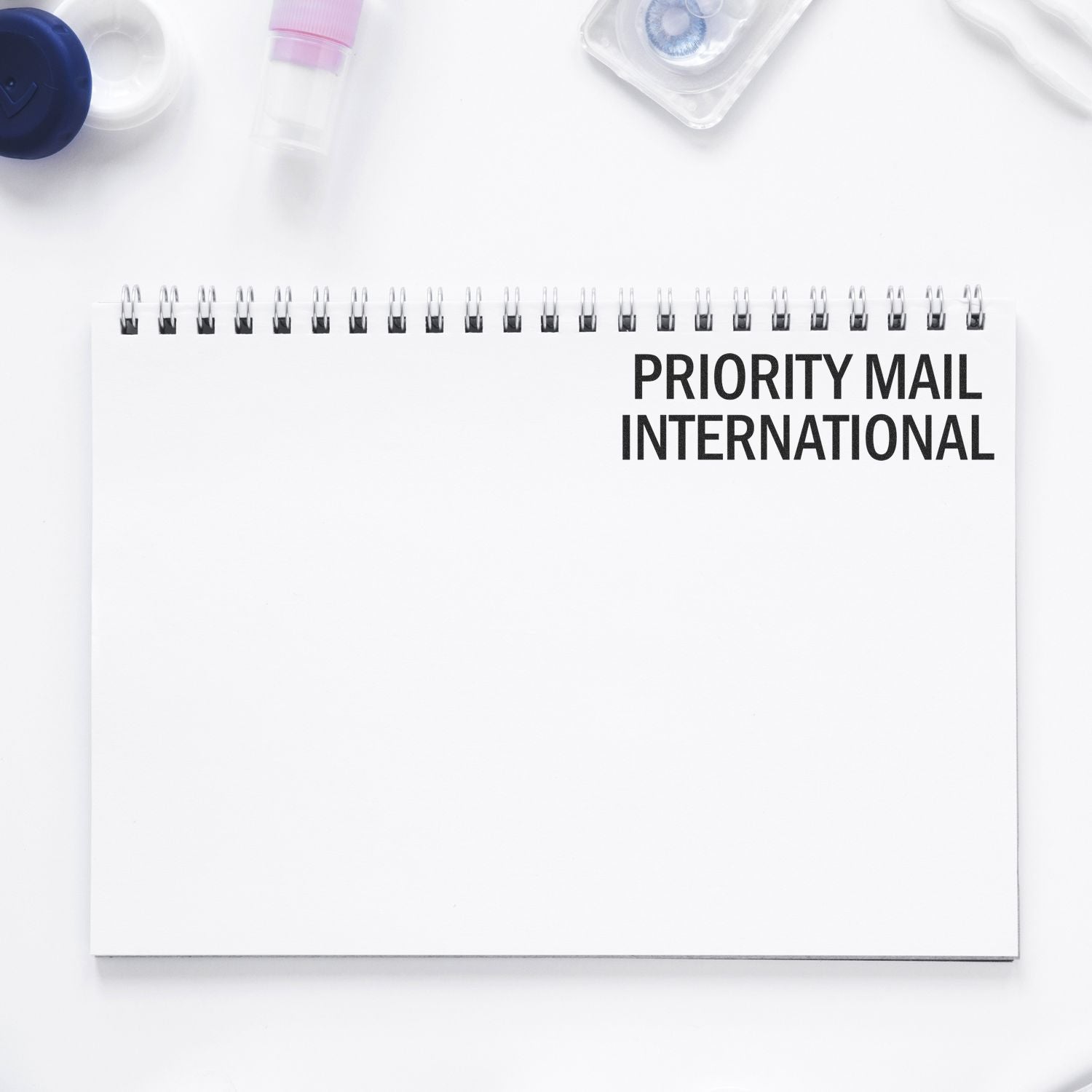 A Large Pre-Inked Priority Mail International Stamp on a white spiral notebook, with office supplies in the background.