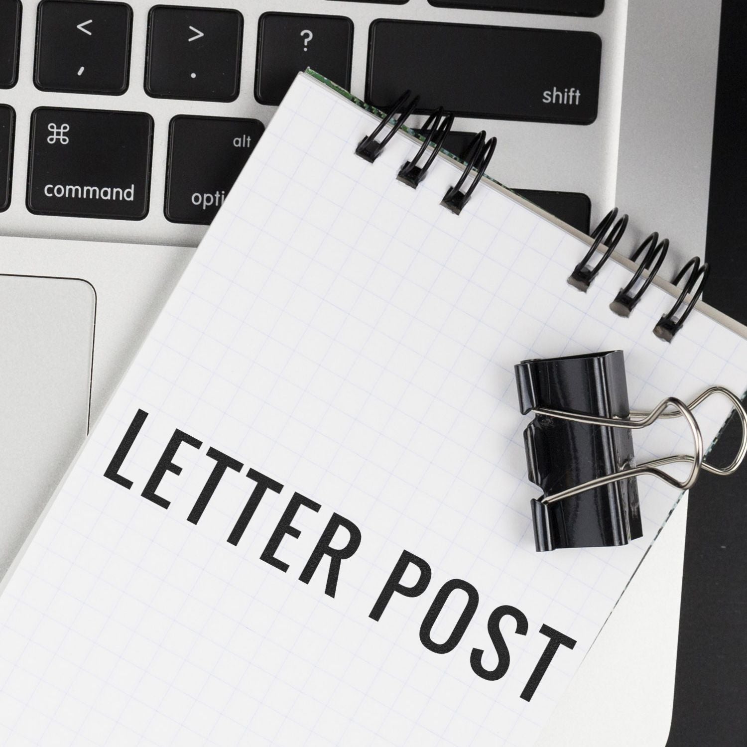 A Large Pre-Inked Letter Post Stamp on a notepad with a binder clip, placed on a laptop keyboard.