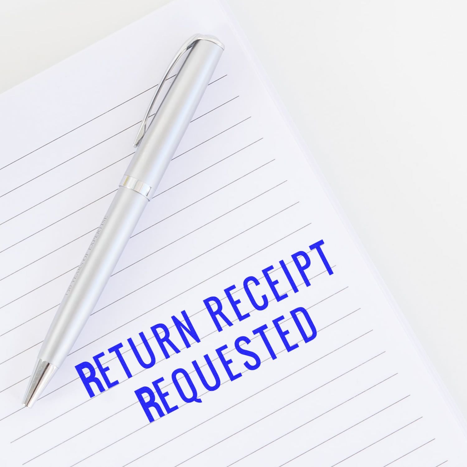 Large Pre-Inked Narrow Font Return Receipt Requested Stamp on lined paper with a silver pen beside it.