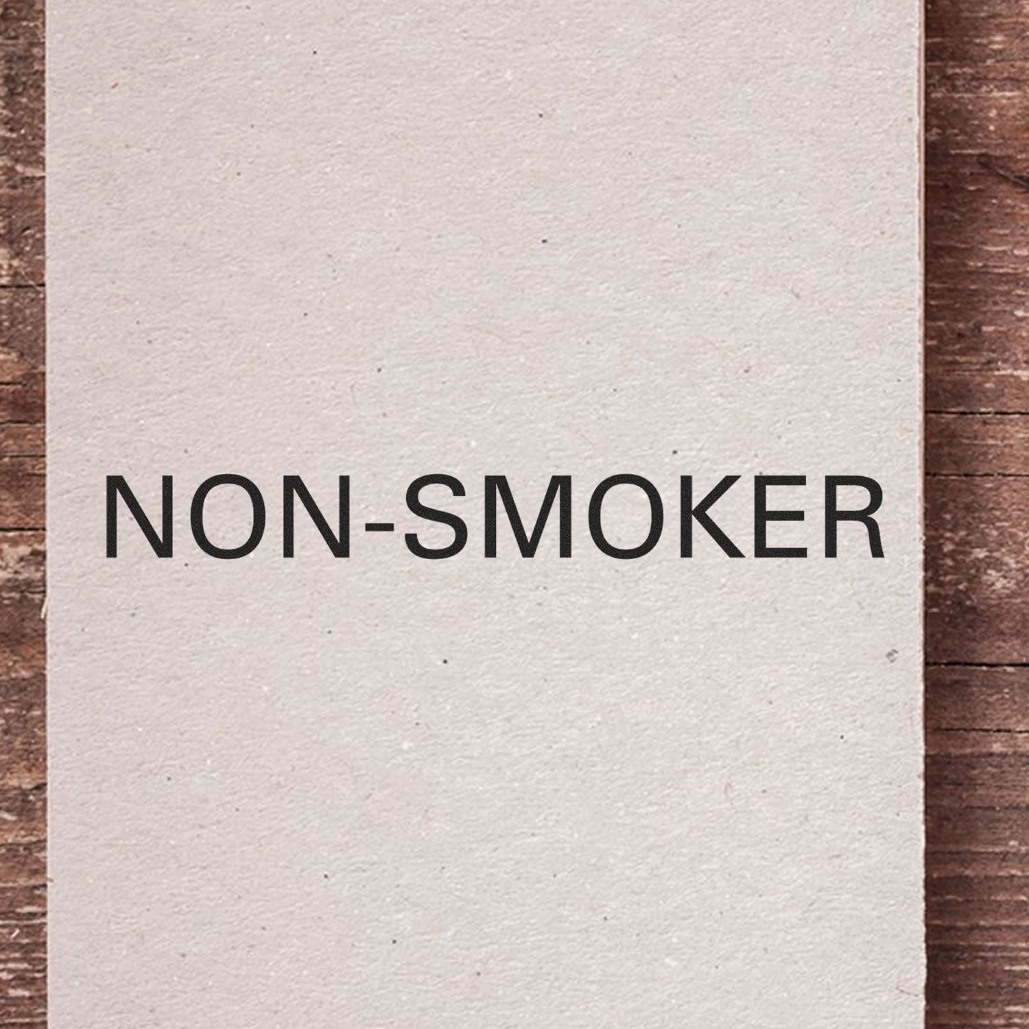 Large Pre-Inked Non-Smoker Stamp with bold black text NON-SMOKER on a white background, placed on a wooden surface.