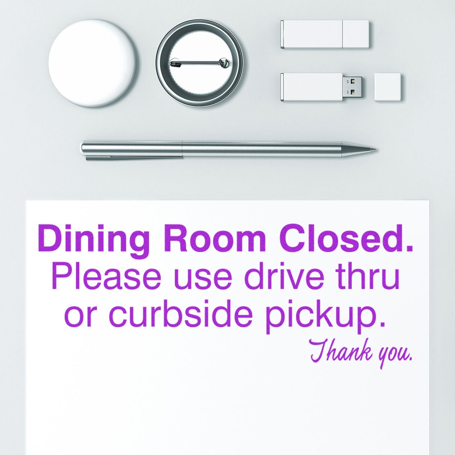 Large Self Inking Dining Room Closed Stamp imprint on paper, surrounded by office supplies including a pen, USB drives, and a badge reel.