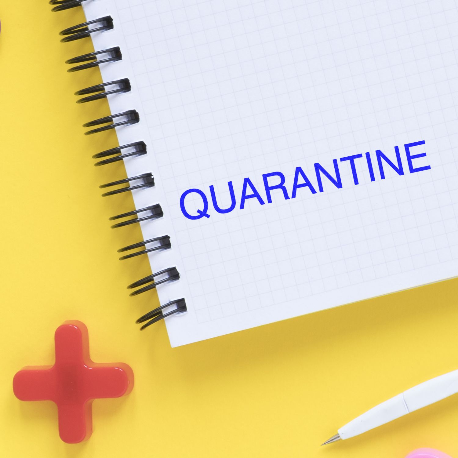 Large Self Inking Quarantine Stamp imprint on a spiral notebook with a yellow background, red cross, and white pen nearby.