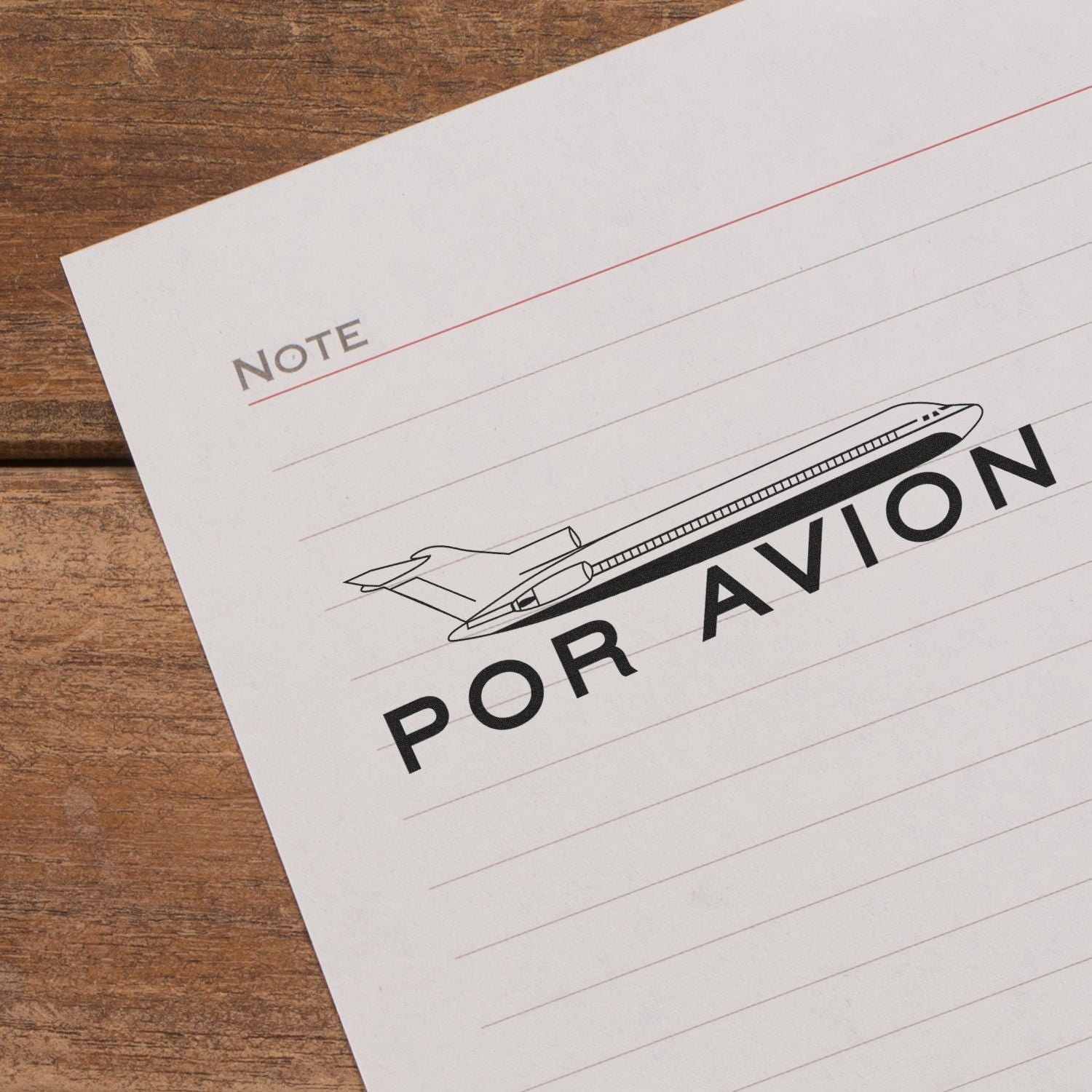 Large Self Inking Por Avion Stamp on a lined paper with a plane illustration and Por Avion text, placed on a wooden surface.