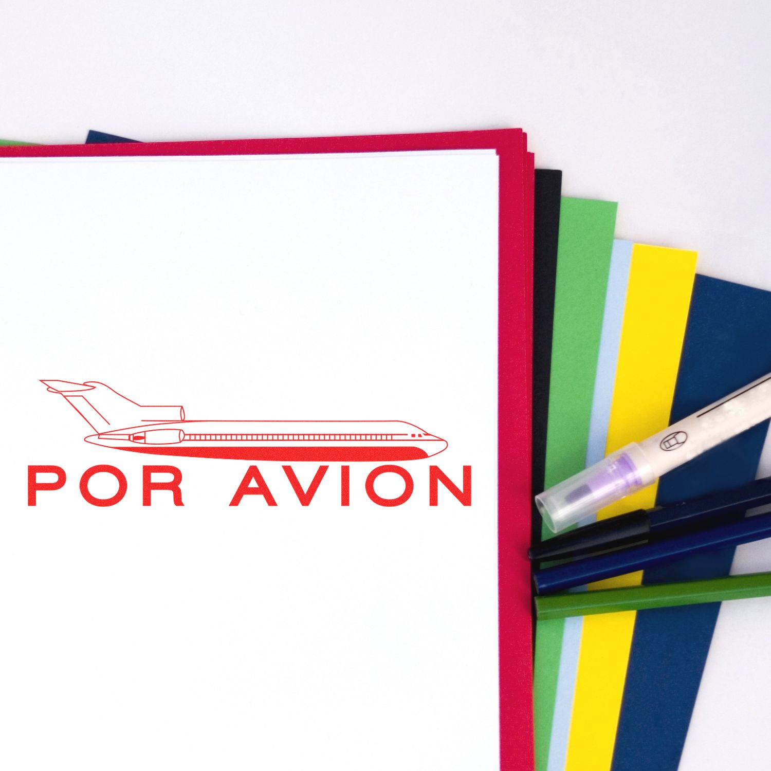 Large Self Inking Por Avion Stamp in red ink on white paper, with colorful sheets and pens in the background.