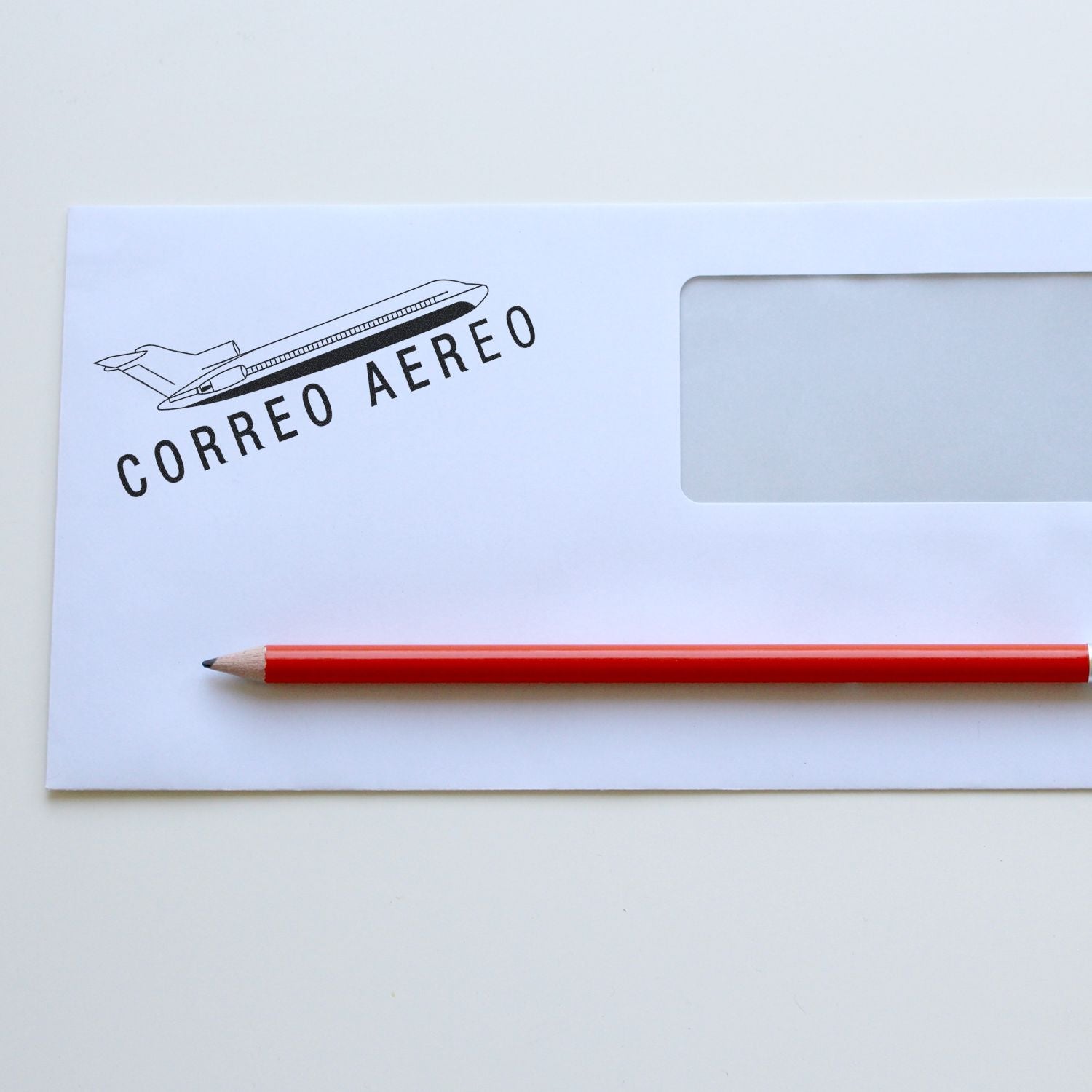 White envelope stamped with Correo Aereo using the Large Self Inking Correo Aero Stamp, placed next to a red pencil on a white surface.