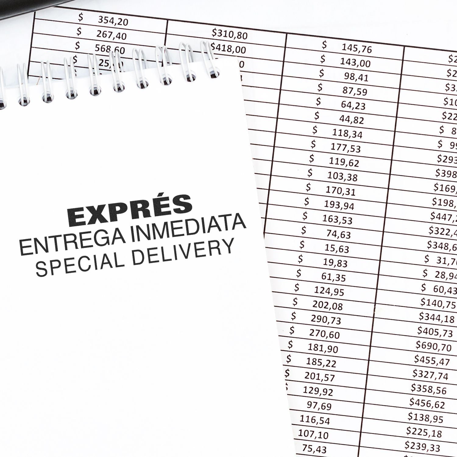 Large Self Inking Expres Entrega Inmediata Stamp on a notepad next to a financial spreadsheet with various dollar amounts.