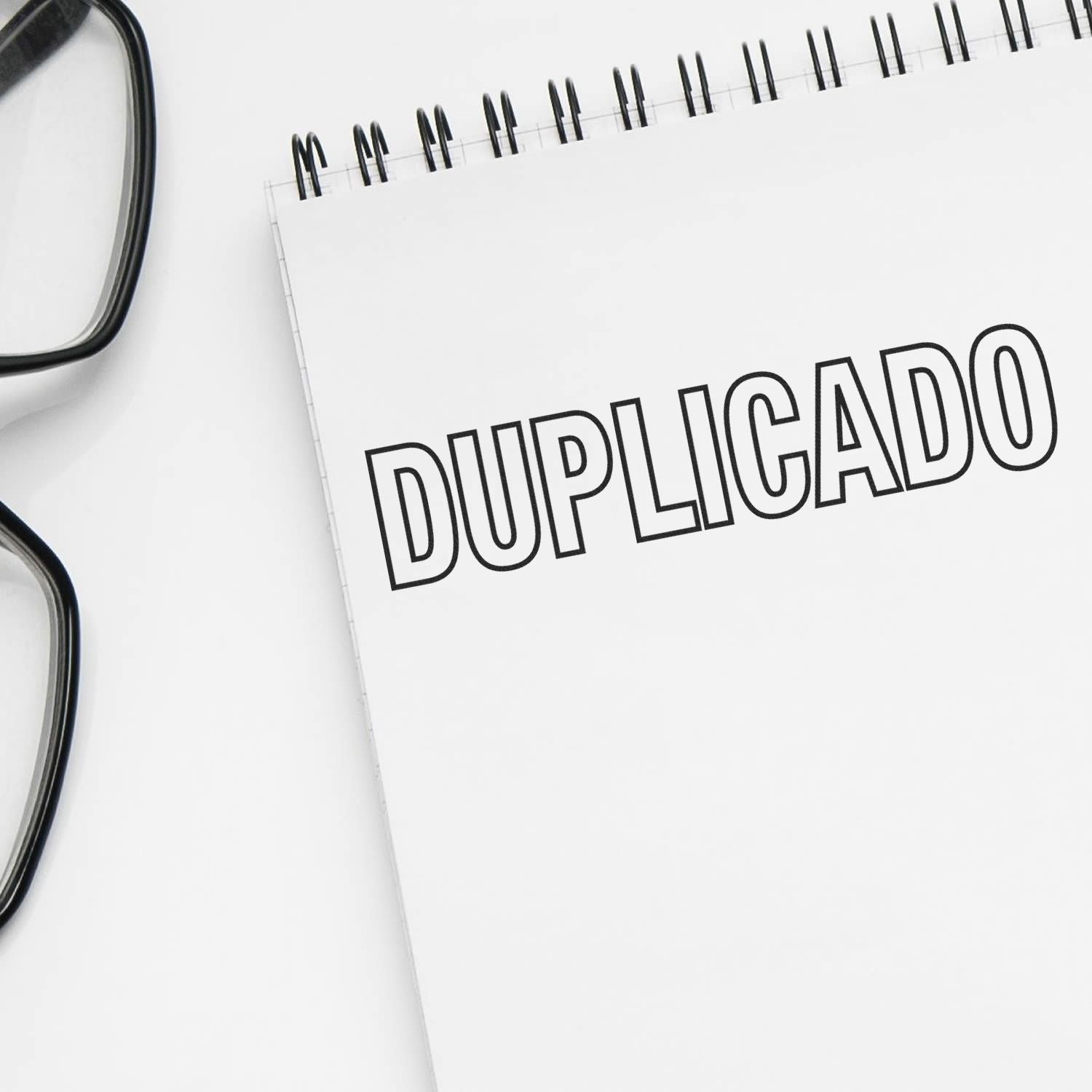 Large Self Inking Duplicado Stamp imprint on a white notepad, with black-rimmed glasses placed beside it.