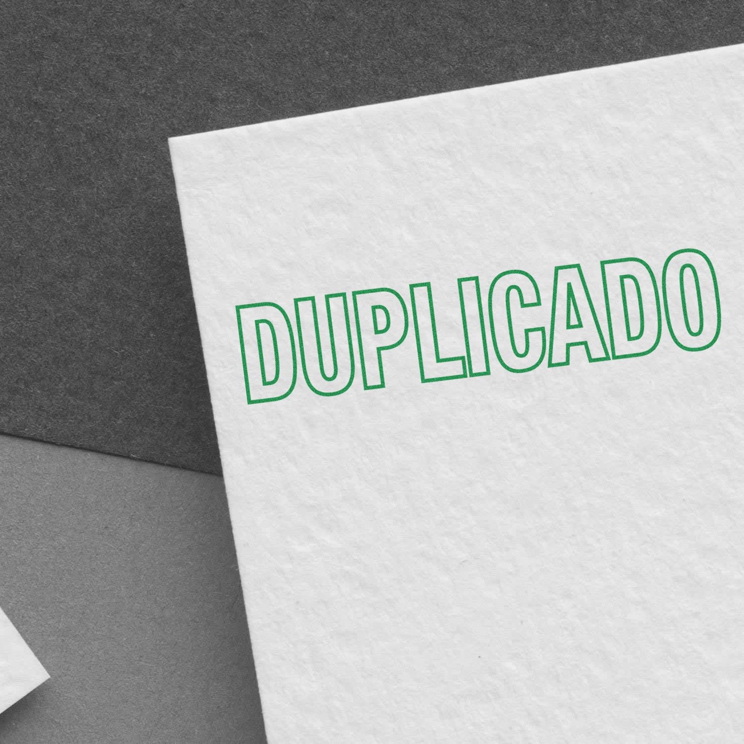 Image of a white paper stamped with DUPLICADO in green ink using the Large Self Inking Duplicado Stamp, placed on a gray surface.