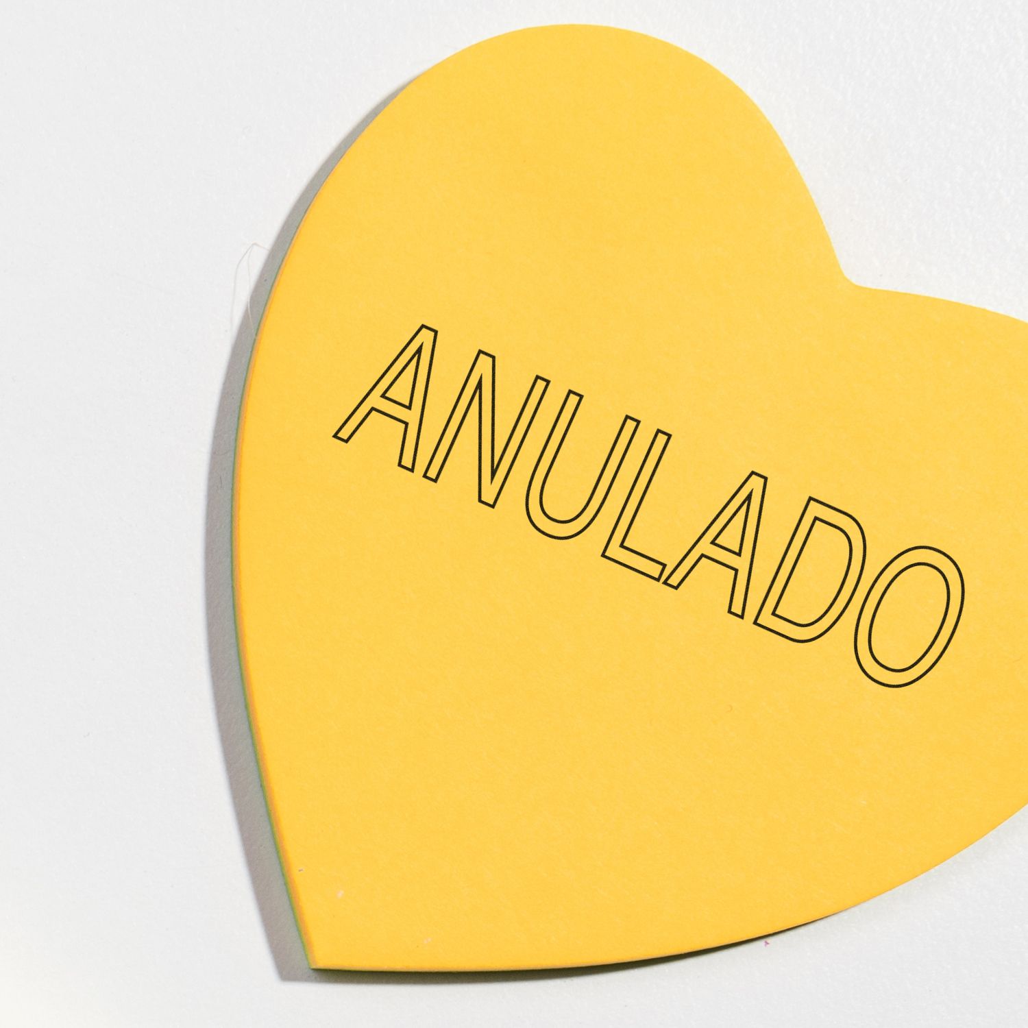 Yellow heart-shaped paper stamped with ANULADO using the Large Self Inking Outline Anulado Stamp, placed on a white background.