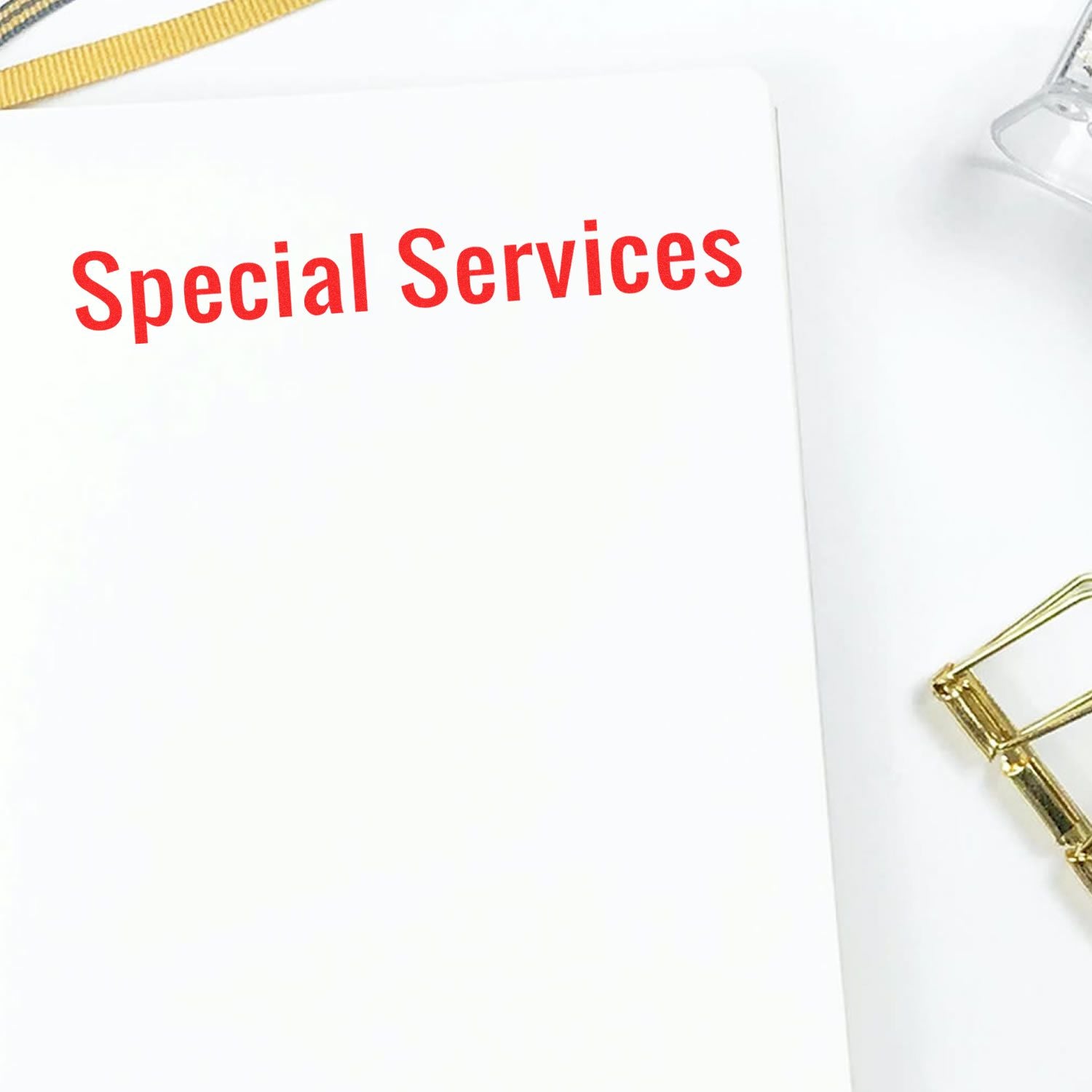 Large Pre-Inked Special Services Stamp in red ink on white paper, with a gold paperclip and a clear plastic item nearby.