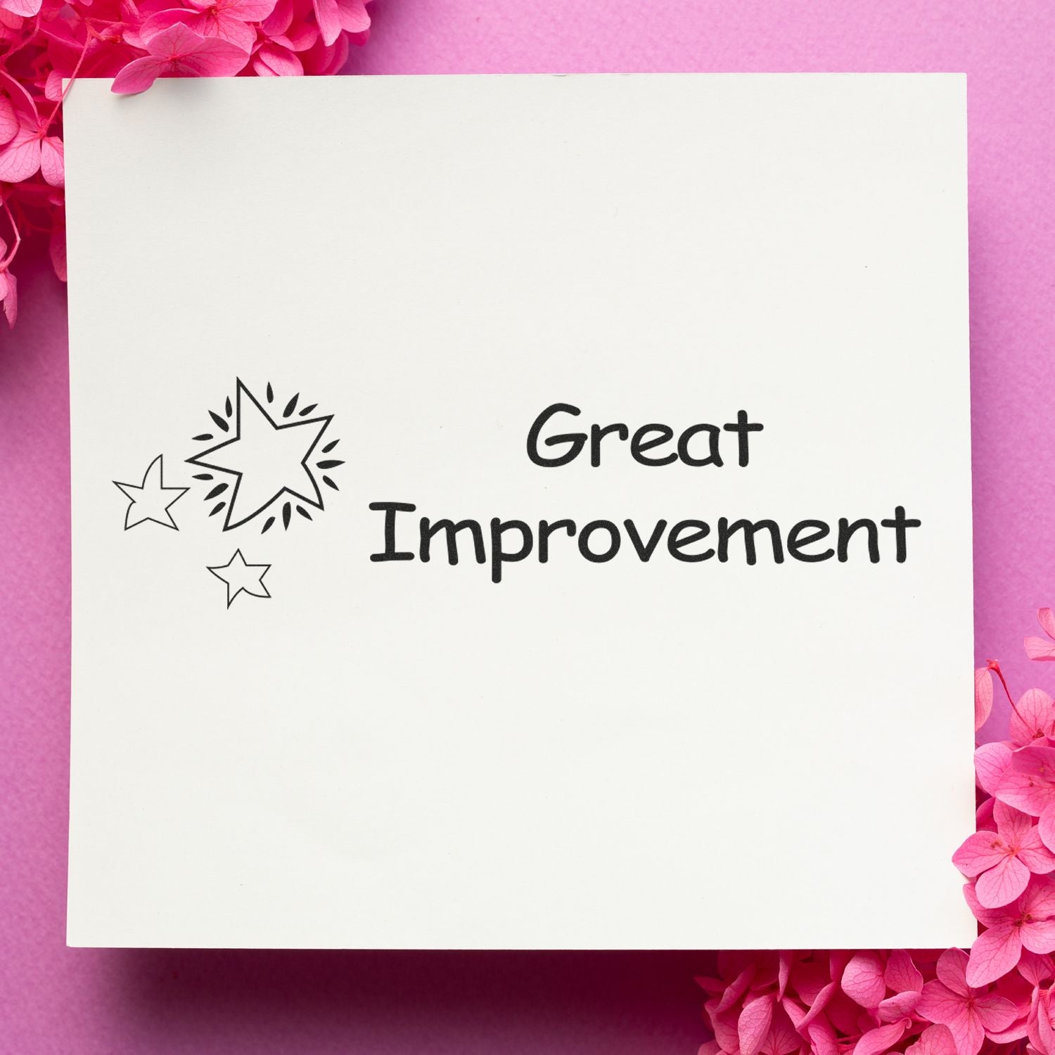 Large Pre-Inked Great Improvement Stamp on white paper with star designs, surrounded by pink flowers on a pink background.