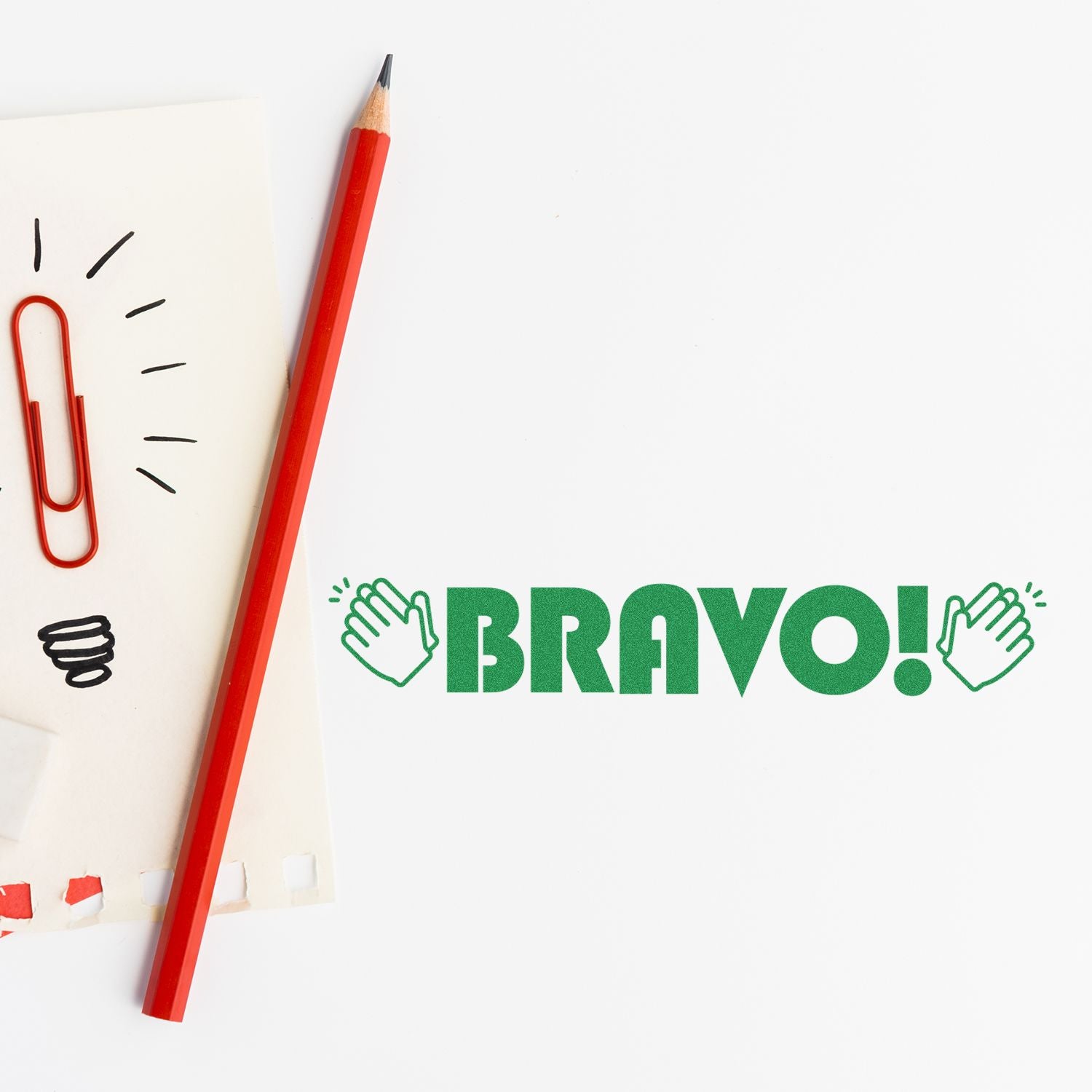 Large Pre-Inked Bravo with Hands Stamp in green ink next to a red pencil, paperclip, and notepad on a white background.