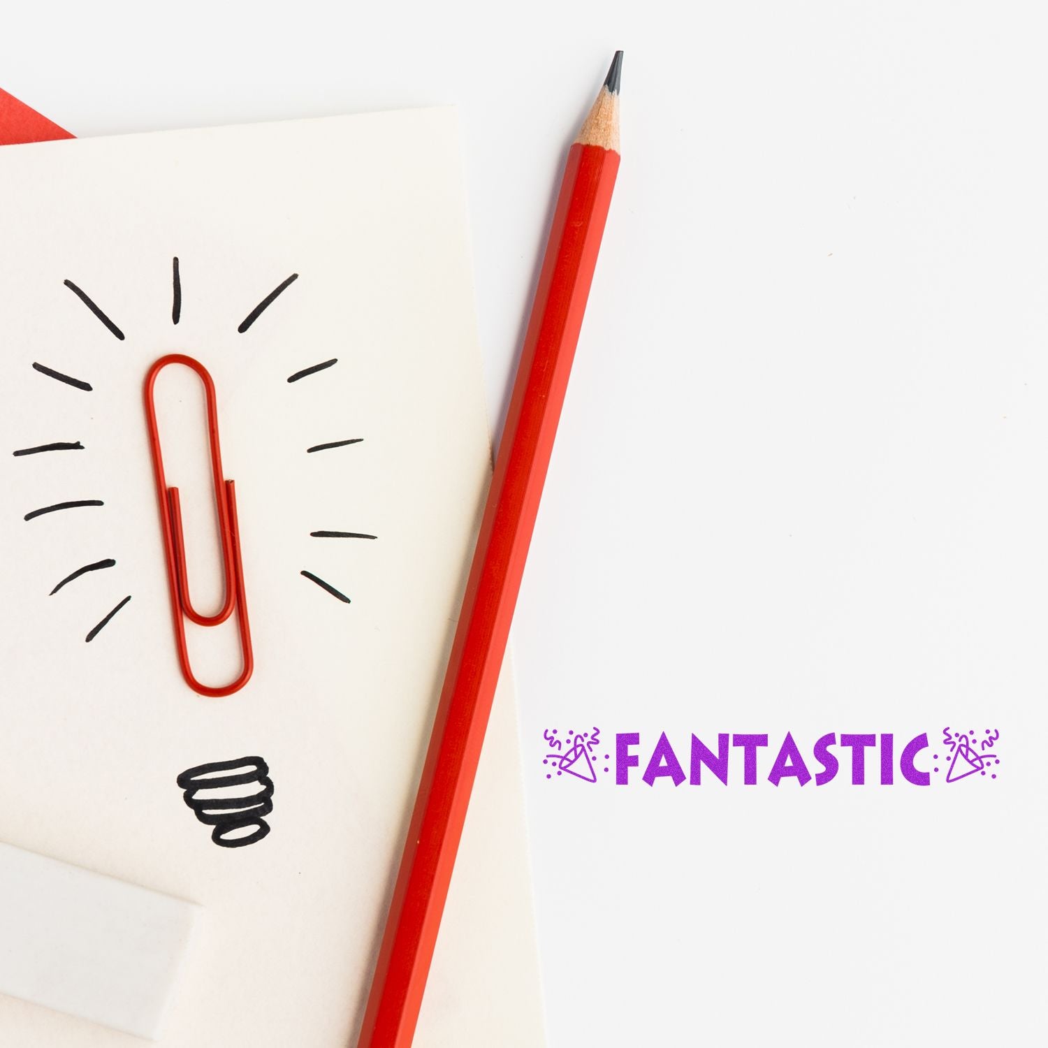 Image of a red pencil and paperclip on a notepad with a lightbulb drawing, next to the Large Pre-Inked Fantastic with Icons Stamp.