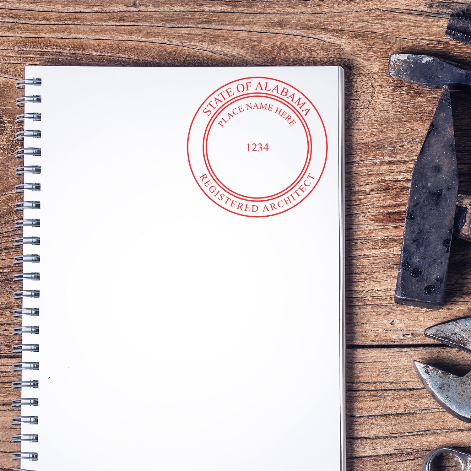 Alabama Architect Seal Stamp on a blank spiral notebook, placed on a wooden table with various tools nearby.