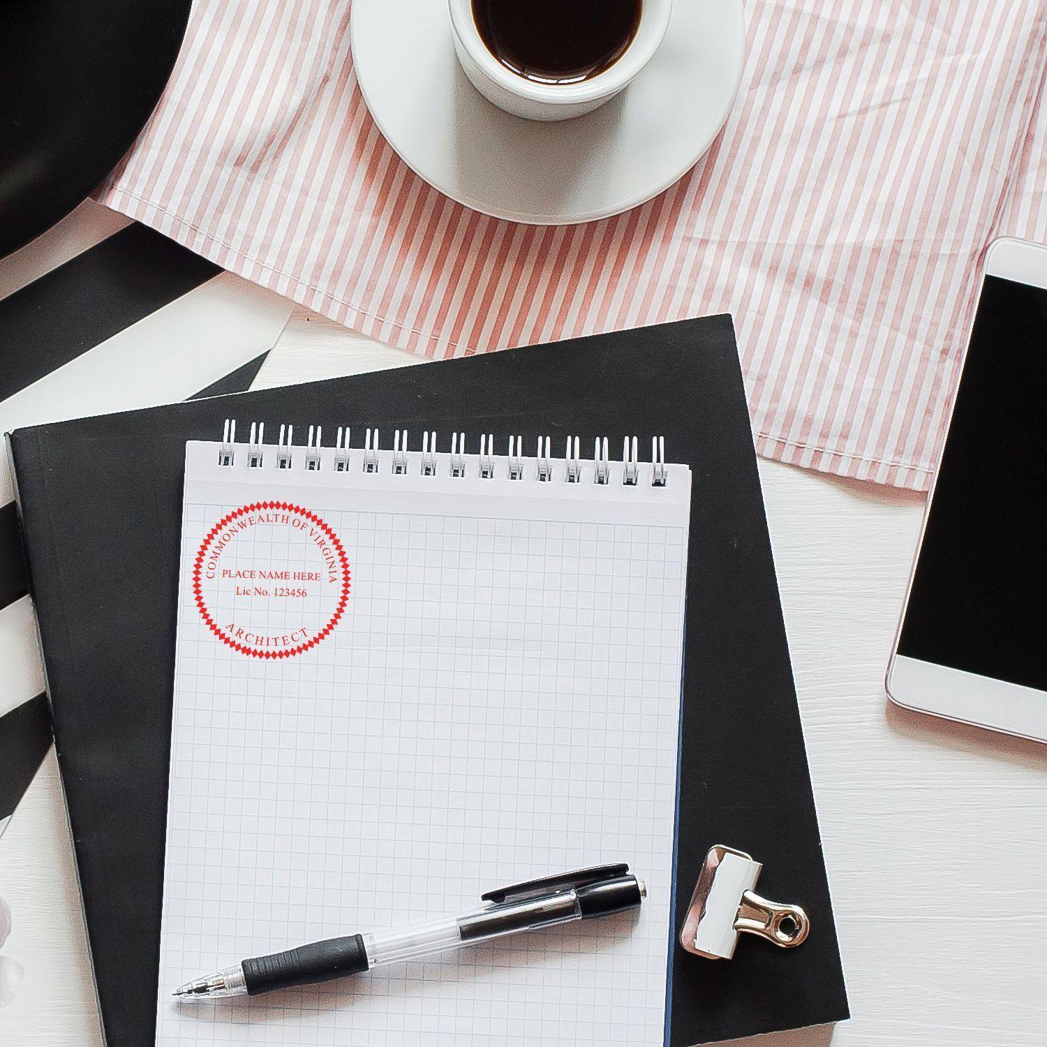 A desk with a cup of coffee, a smartphone, and a notepad stamped with the Architect eSeal Electronic Image Stamp of Seal. The stamp is red and circular, placed on the top left corner of the notepad.