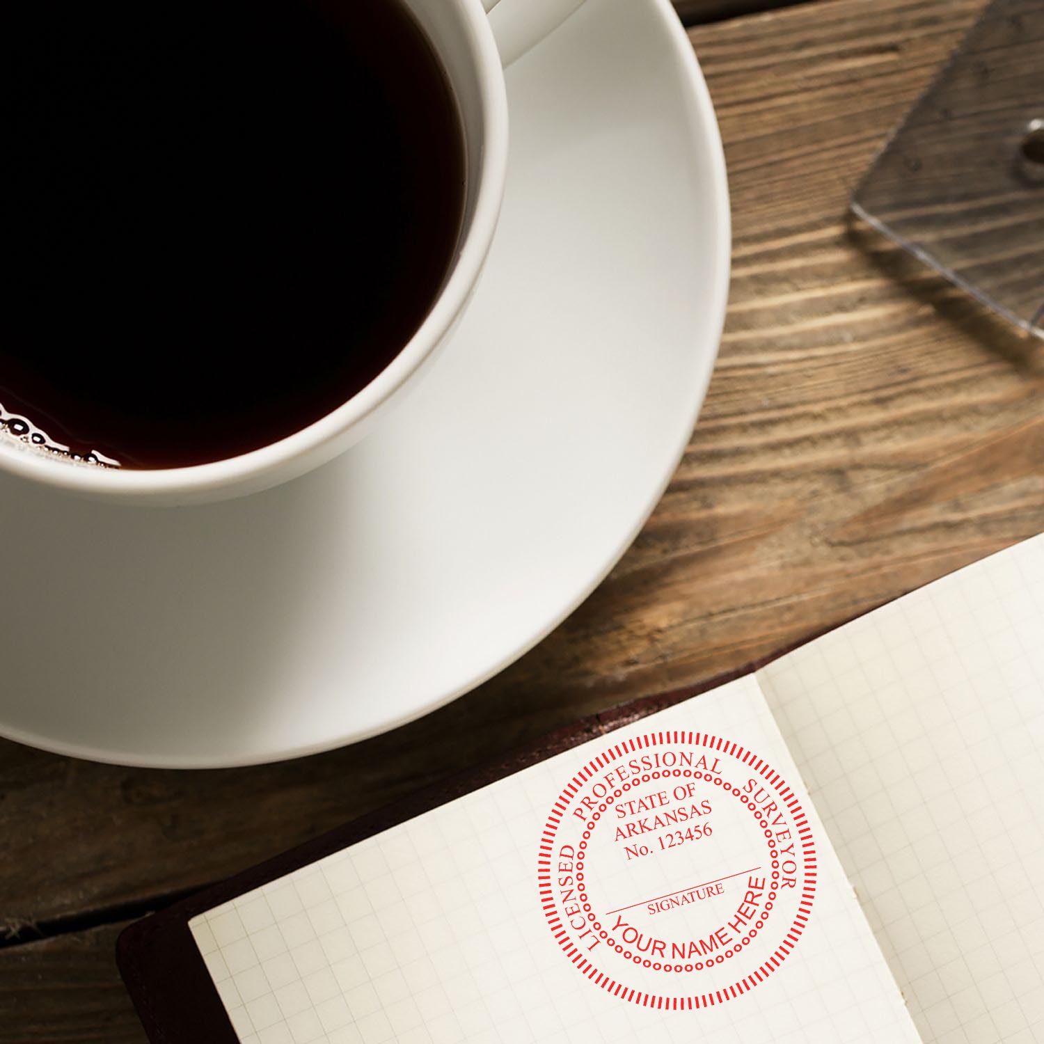 Self Inking Arkansas Land Surveyor Stamp imprint on paper next to a cup of coffee on a wooden table.